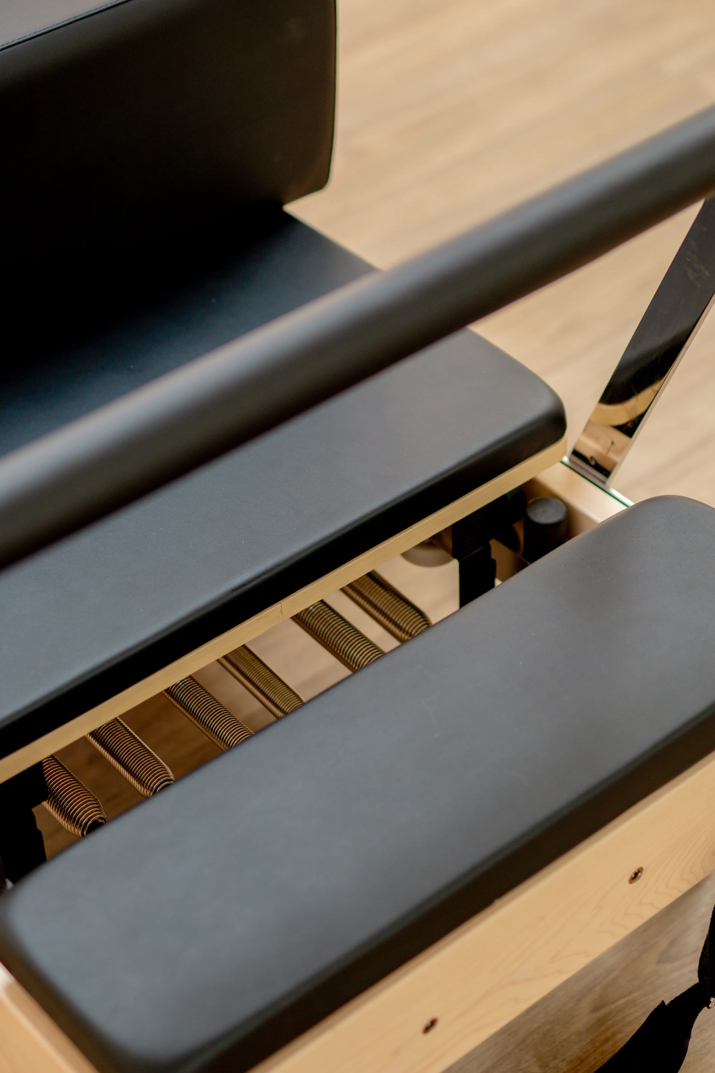 Close-up of a modern piano bench with black cushioned seat and a wooden frame.