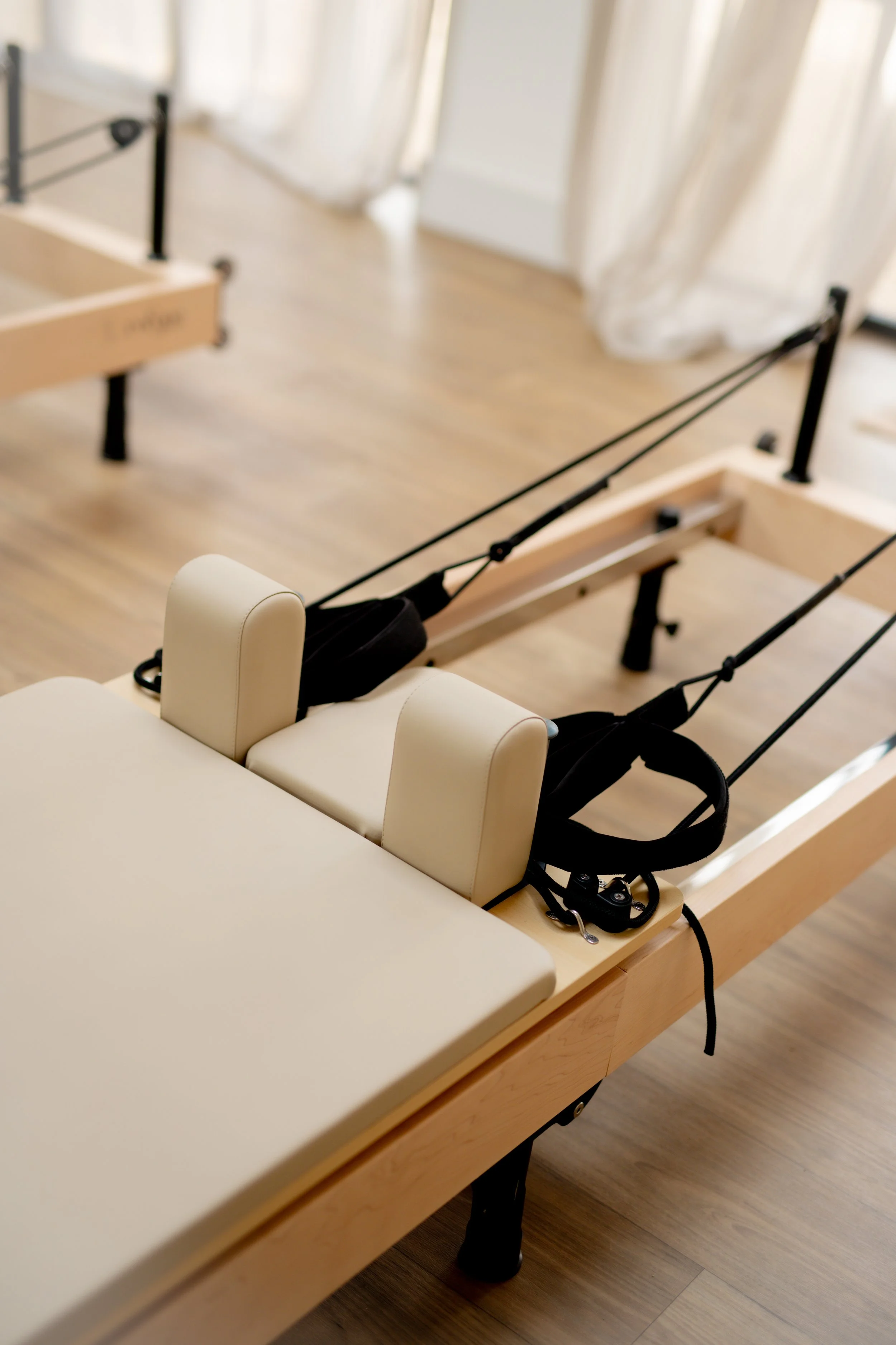 A physical therapy reformer with a padded platform and adjustable straps in a well-lit room with curtains and hardwood floors.