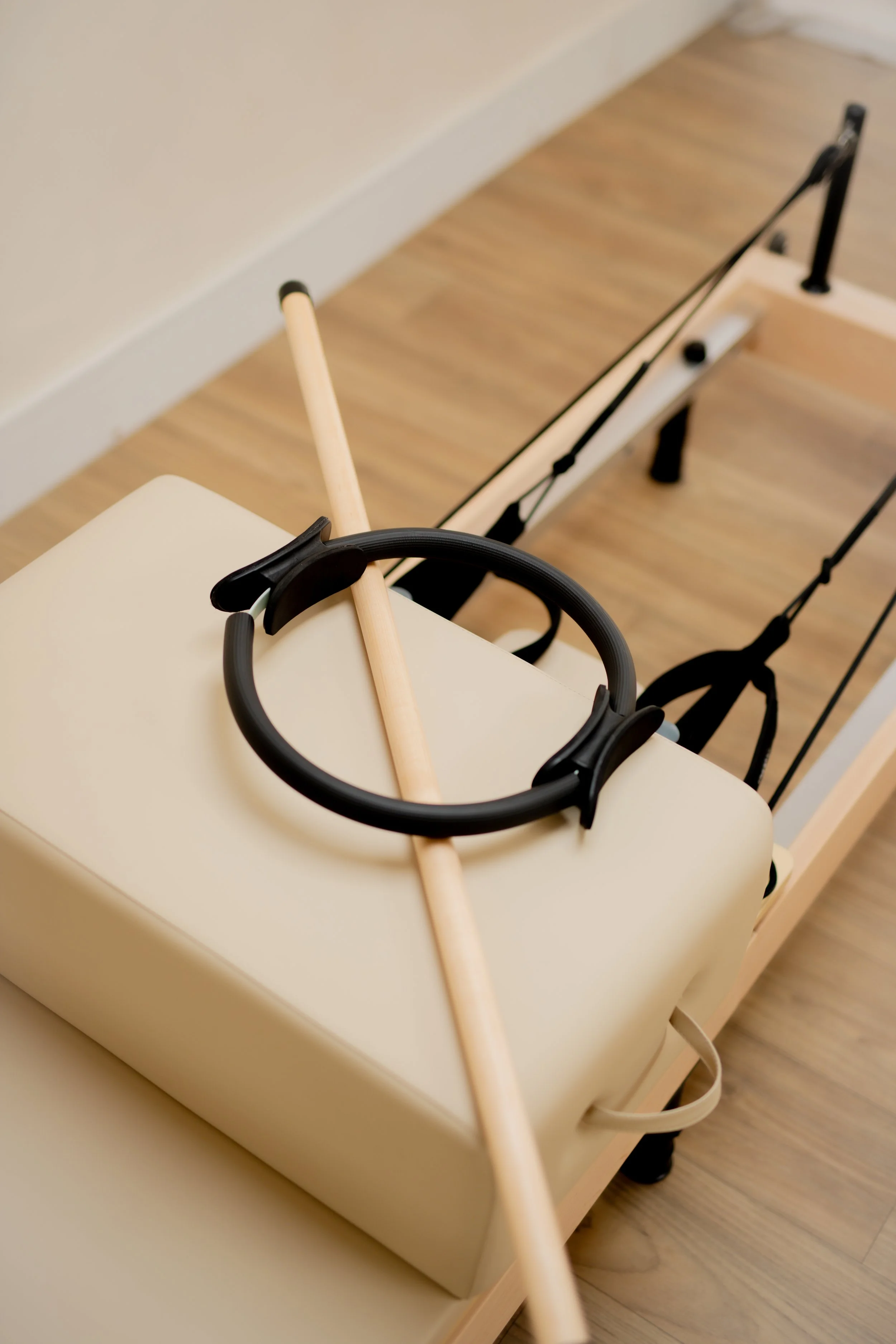 Physical therapy reformer machine with wooden and metal bars, straps, and a foam cushion, located in a room with wooden flooring.