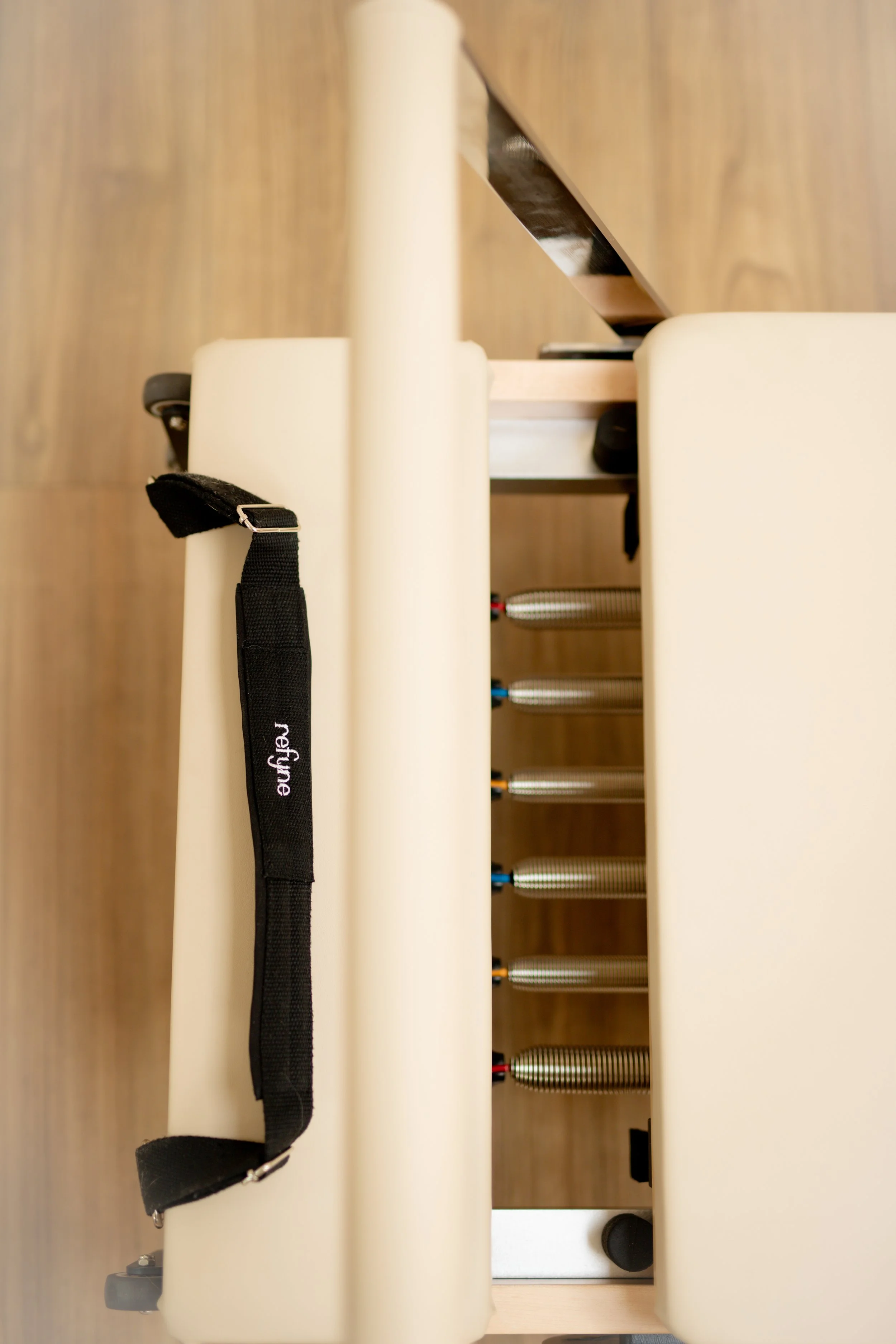Top view of a beige massage table with five silver spring coils showing underneath and a black strap hanging on the left side.