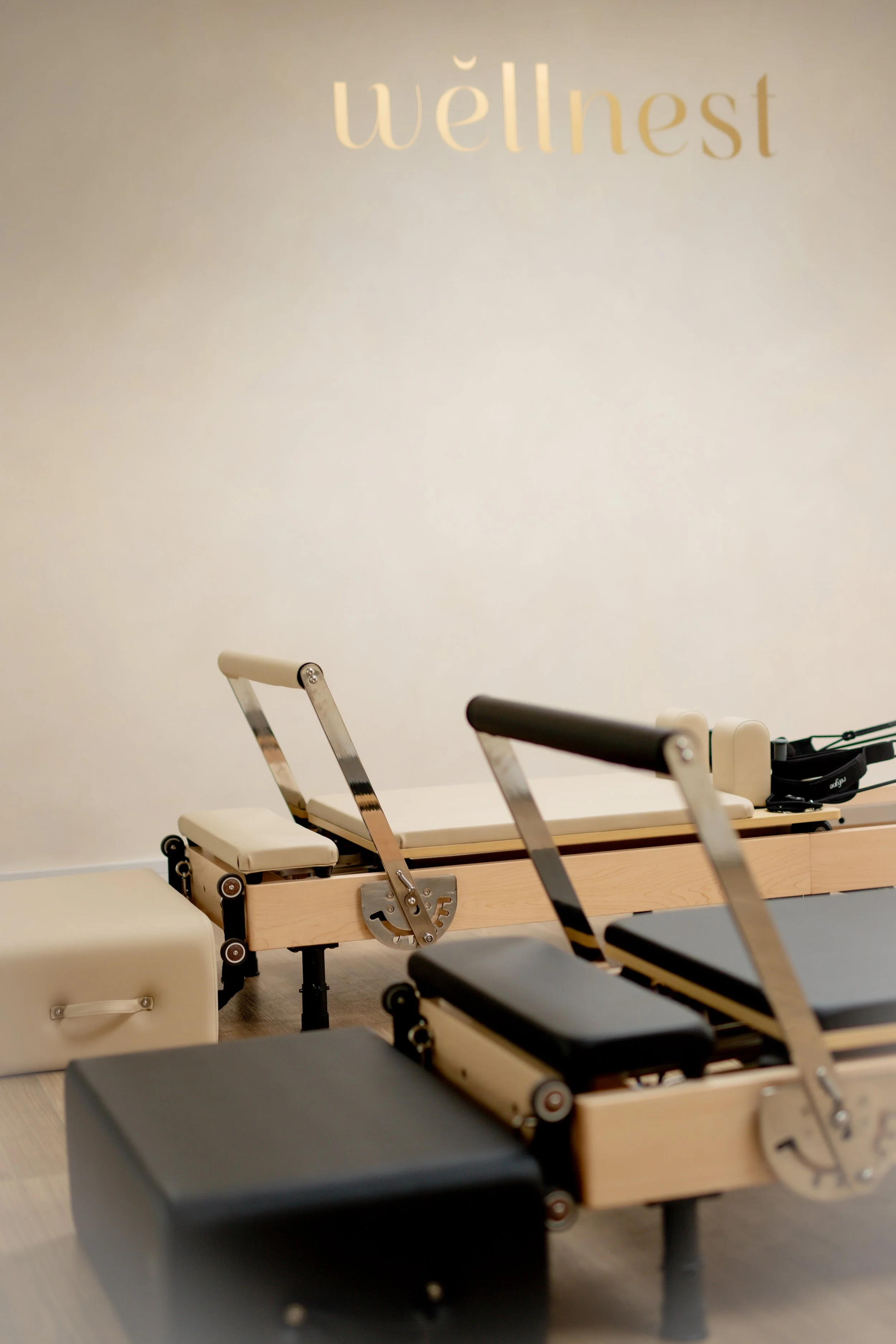 Reformer Pilates machines in a wellness studio with a sign reading 'wellnest' on the wall.