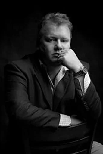 Portrait of a man with a thoughtful expression, resting his chin on his hand, in black and white.