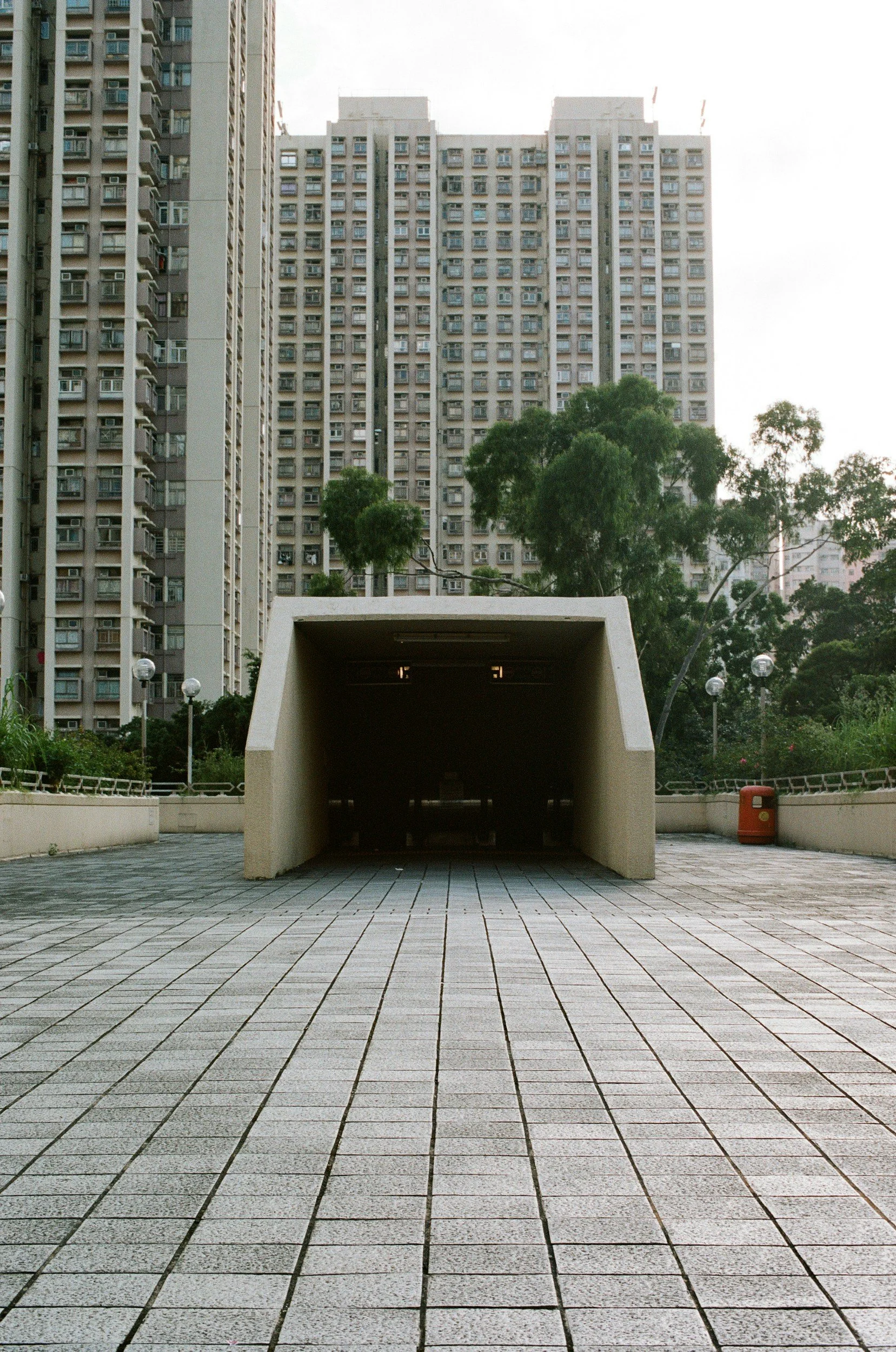 Empty underground pedestrian tunnel in an urban park with tall residential buildings and trees in the background.