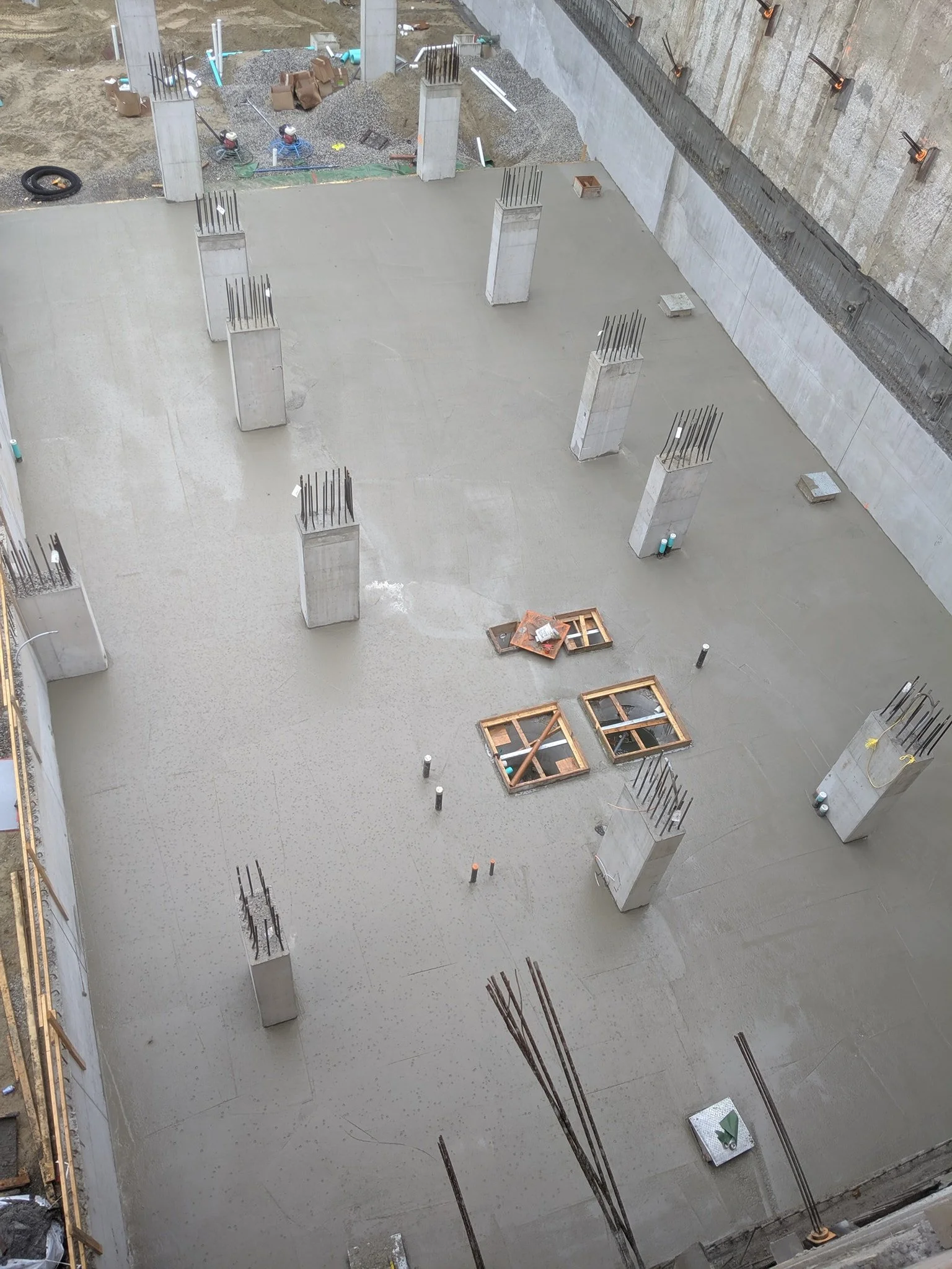 Construction site with concrete floor, multiple concrete columns with rebar, and wooden frames for future openings.