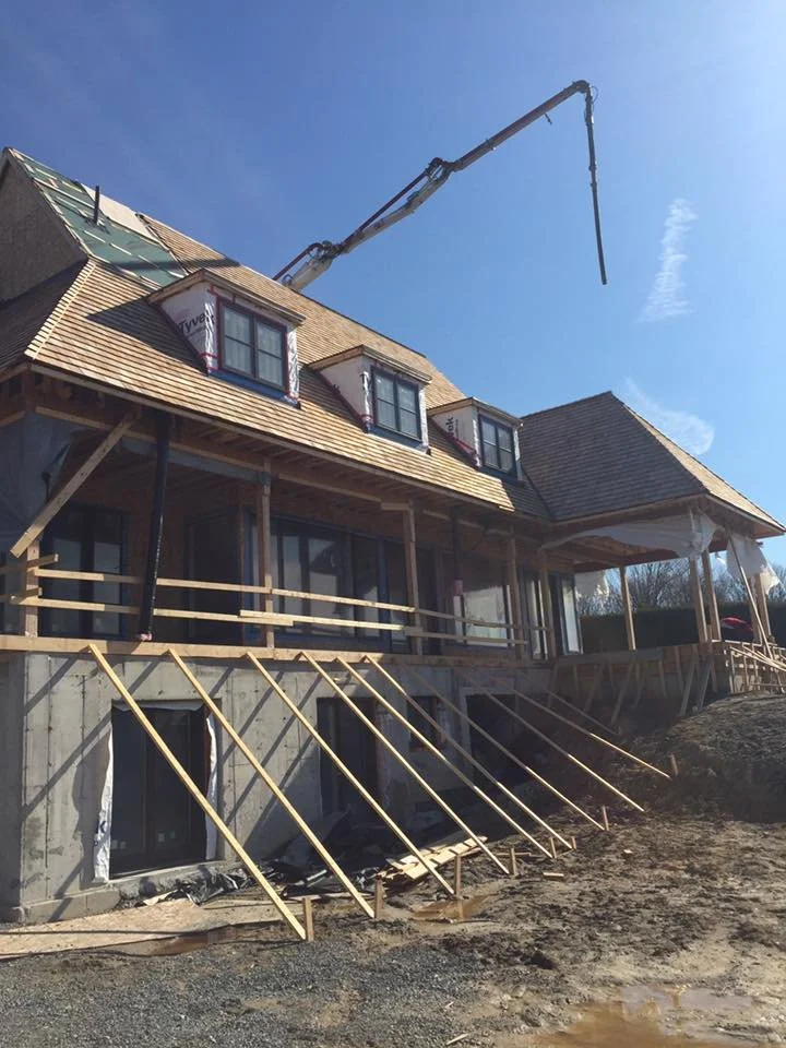 Construction site of a house with a crane and wooden supports in place for roof installation, viewed from ground level with clear blue sky in the background.