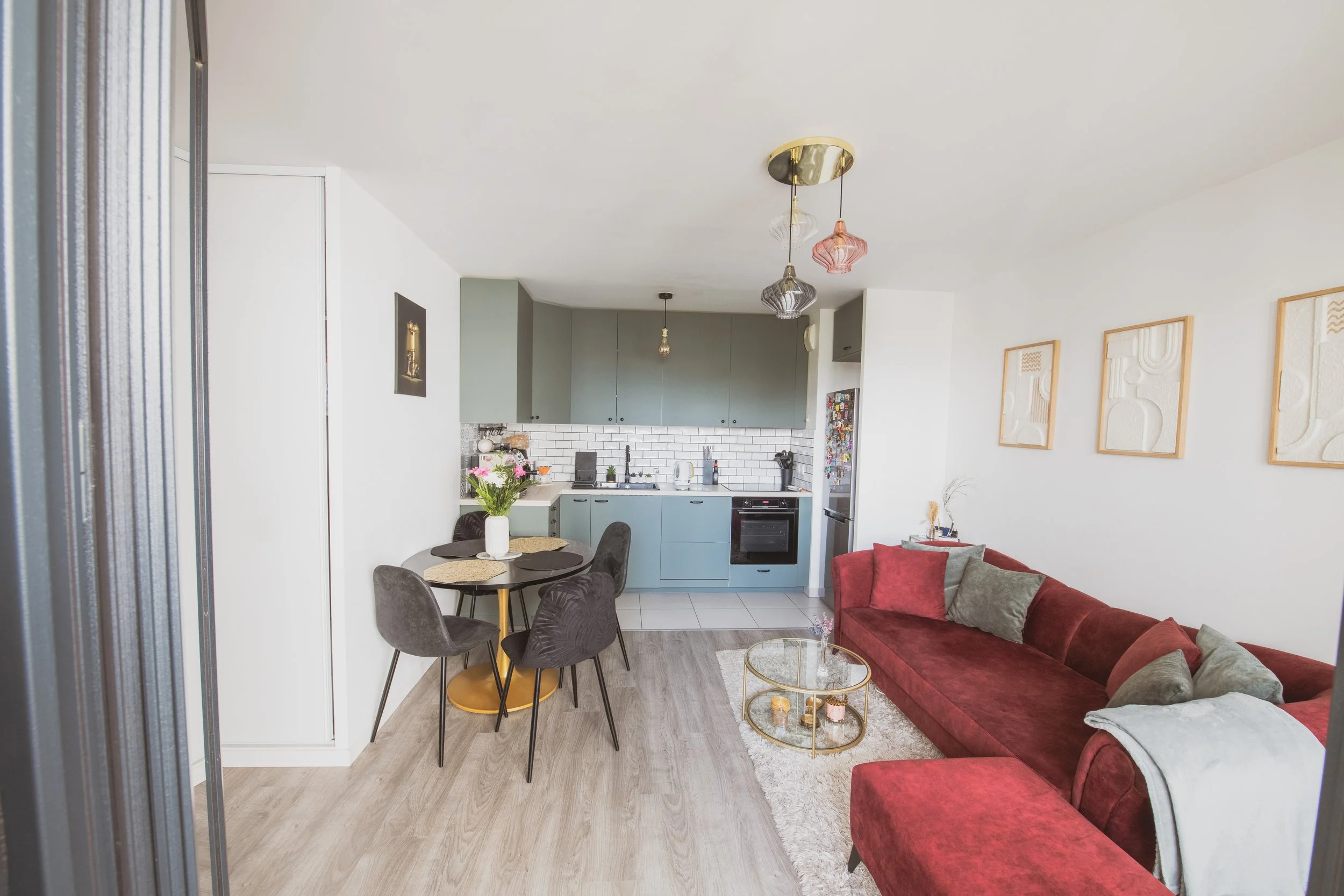 Salon et cuisine dans un appartement moderne avec un canapé rouge, table basse, cuisine gris-vert, petites décorations et plantes