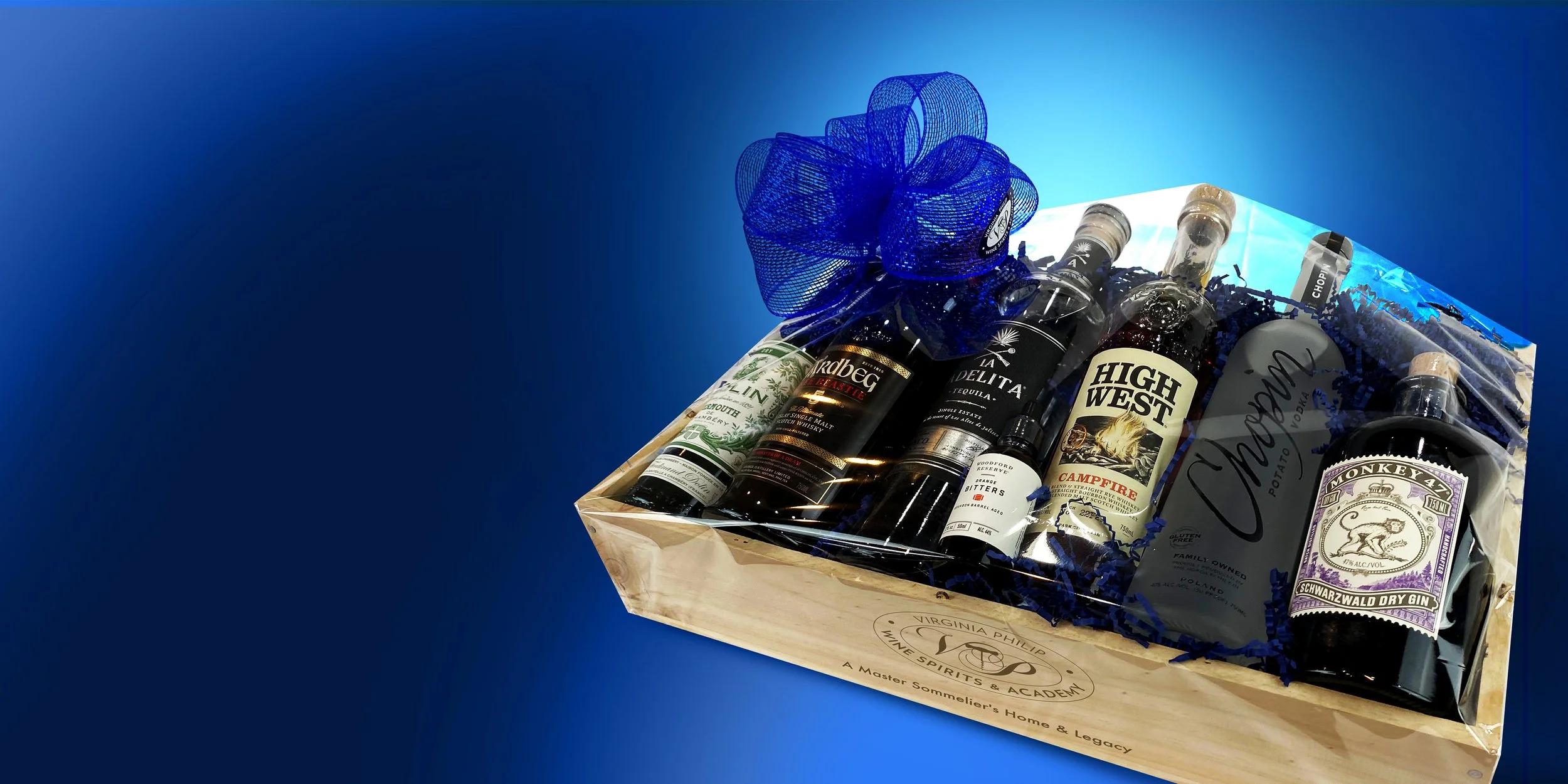 A gift box containing various bottles of spirits, including gin, tequila, and whiskey, wrapped in cellophane with a blue ribbon on top.