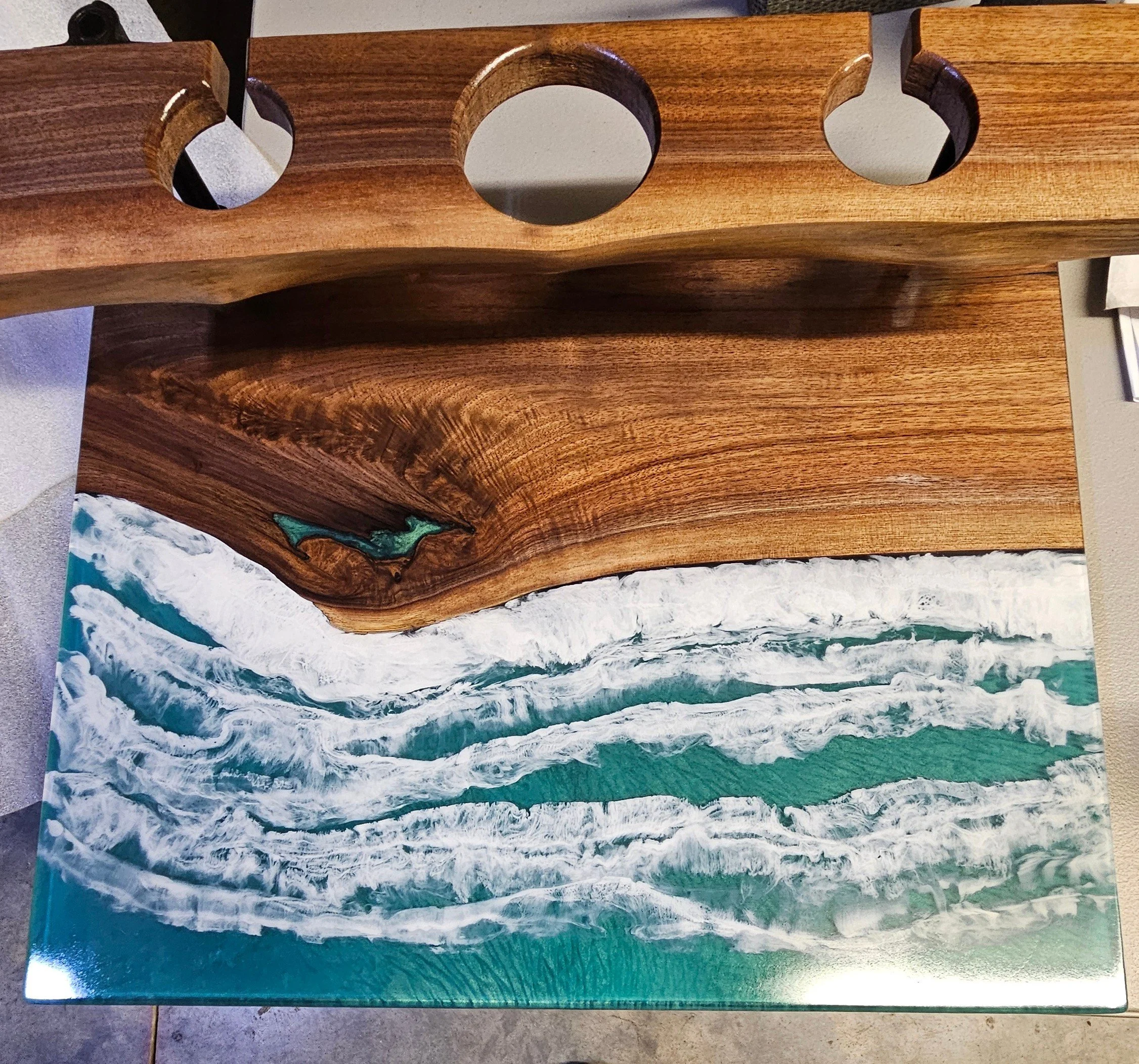 A coastal scene featuring an ocean with white waves crashing on the shore and a long piece of polished wood with a small carved dolphin attached to it.