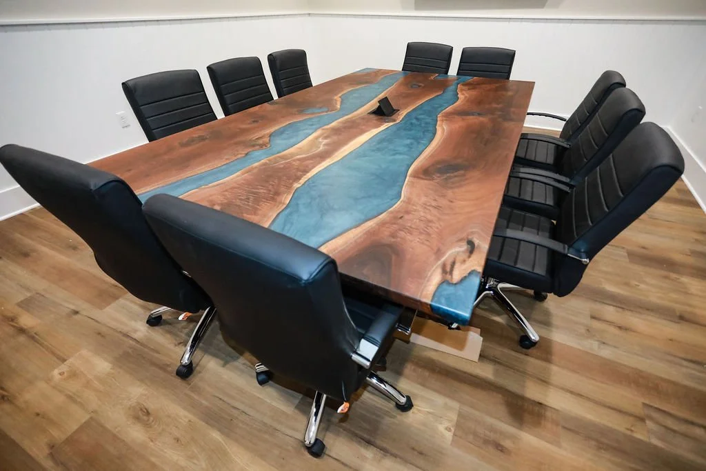 A 10 foot x 5.5 foot walnut conference table with Carolina Blue epoxy rivers and a built-in electronics hub.