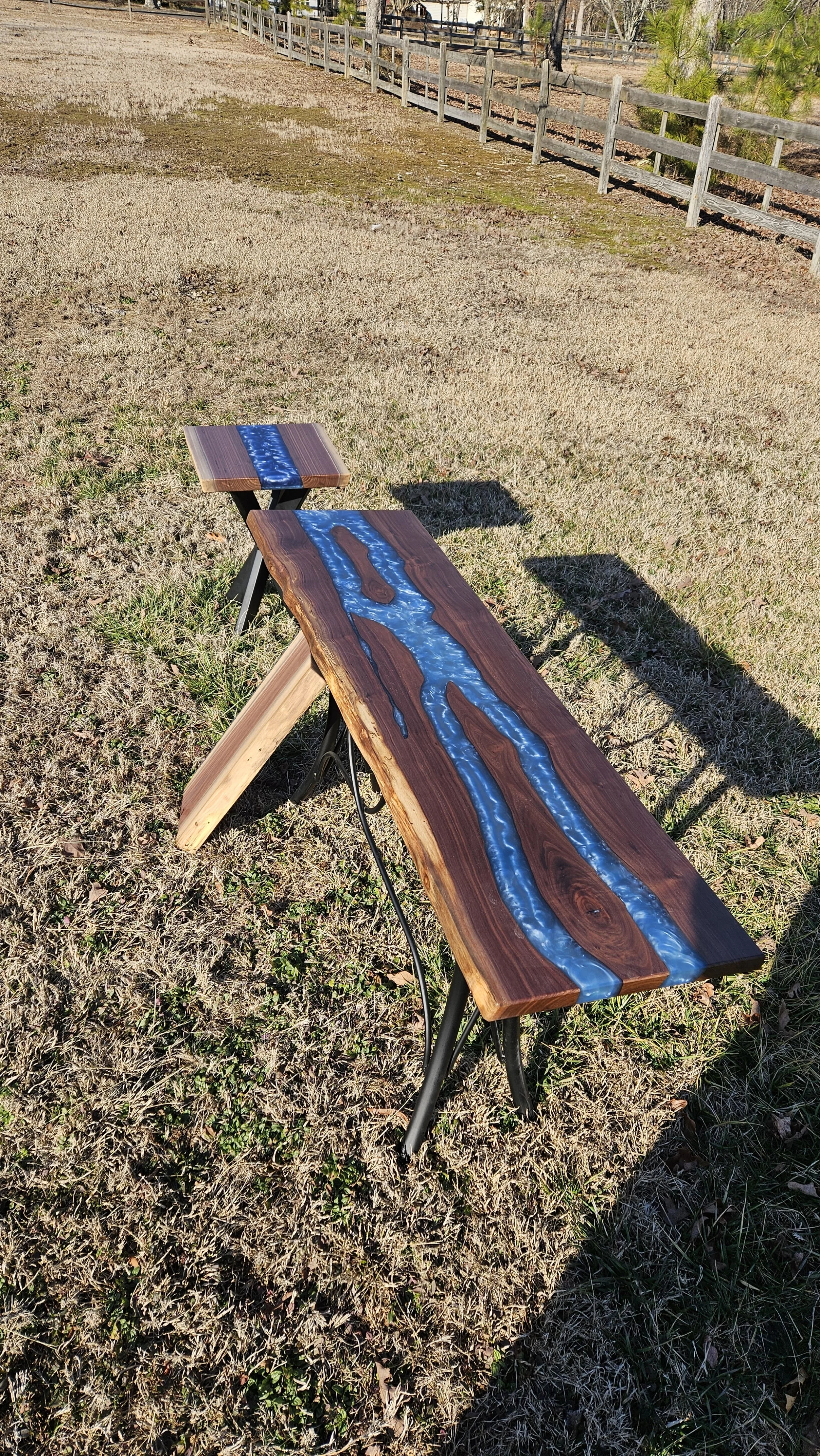 Wooden outdoor table with blue resin river design on a grassy area.