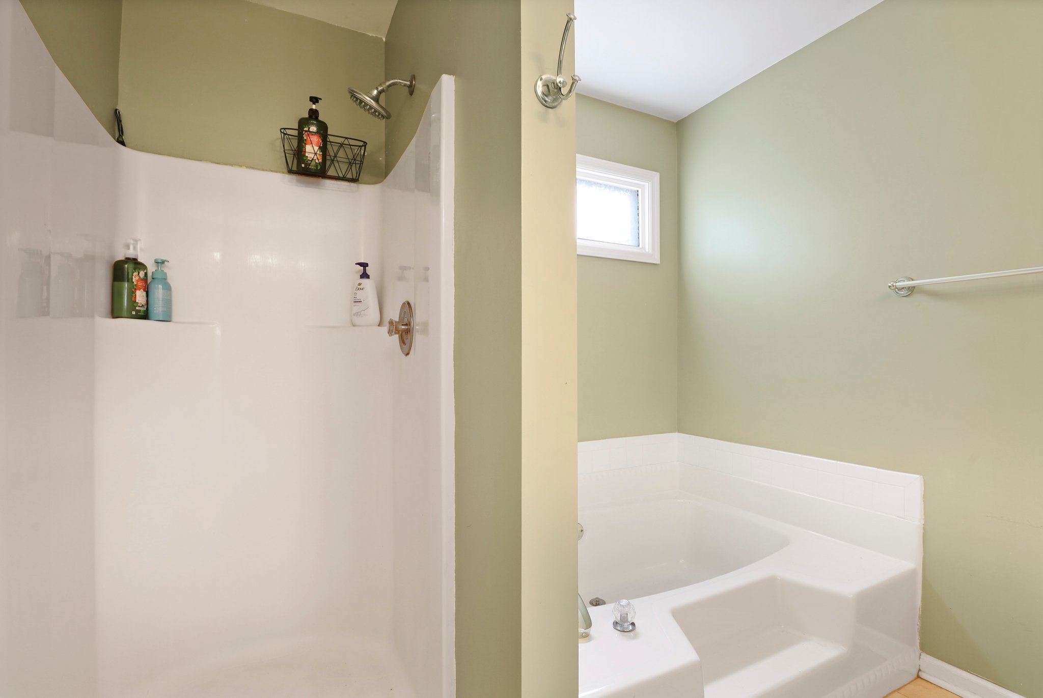 Bathroom with a green wall, a white shower area with various bottled products, and a separate white bathtub.