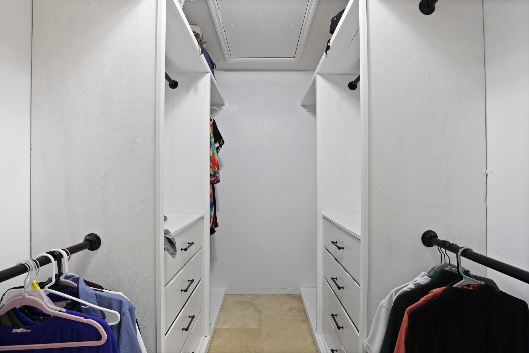 Walk-in closet with white shelving, drawers, and hanging clothes on black rods.