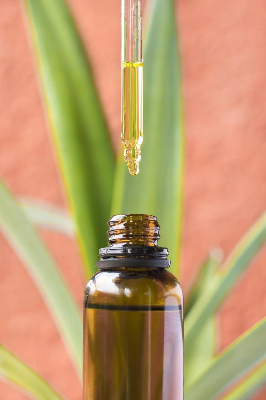 Close-up of a dropper releasing liquid into an amber glass bottle with green leaves in the background.