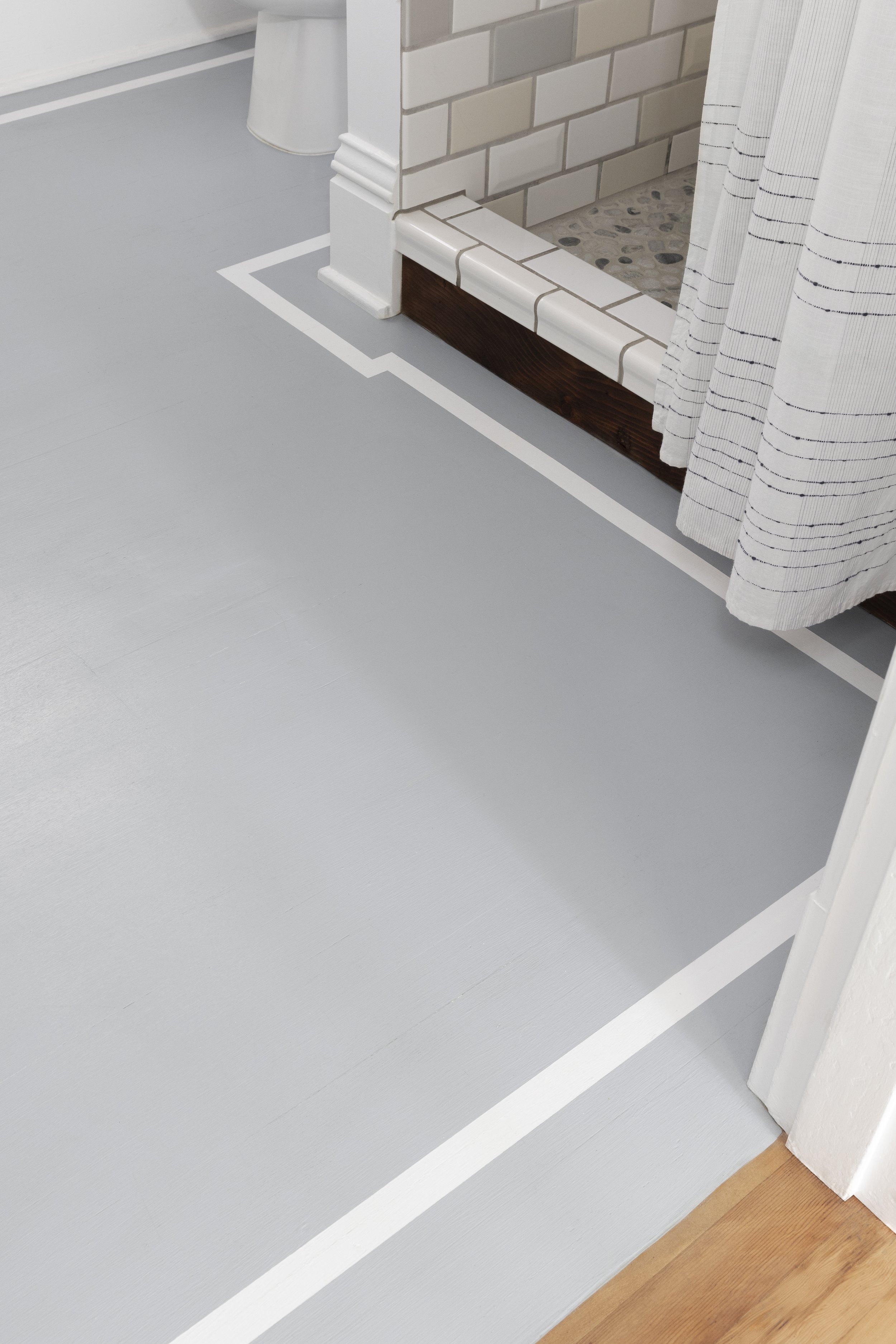 Bathroom interior with light gray flooring, white border, shower area with tile edging, and white shower curtain.