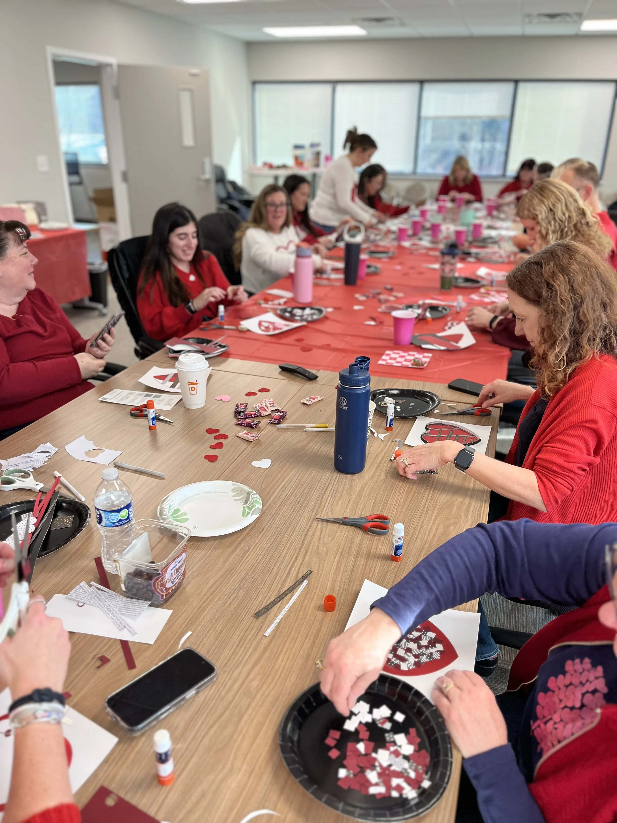 A group of women gathered around a large table, engaged in paper art with paper cutouts and supplies.