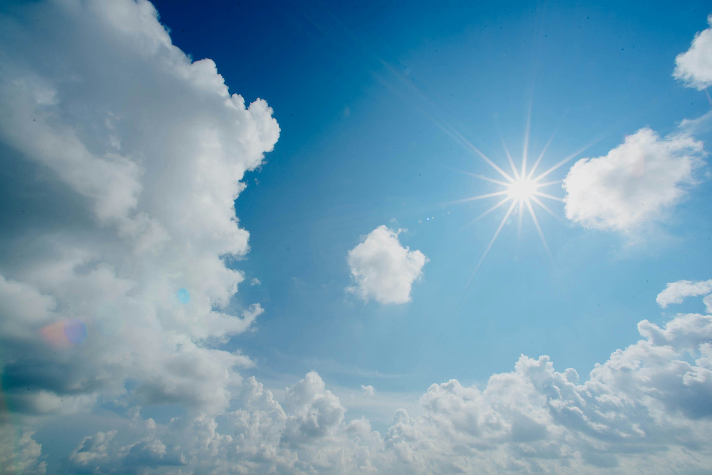 Bright sunlight streaming through a sky filled with fluffy white clouds.