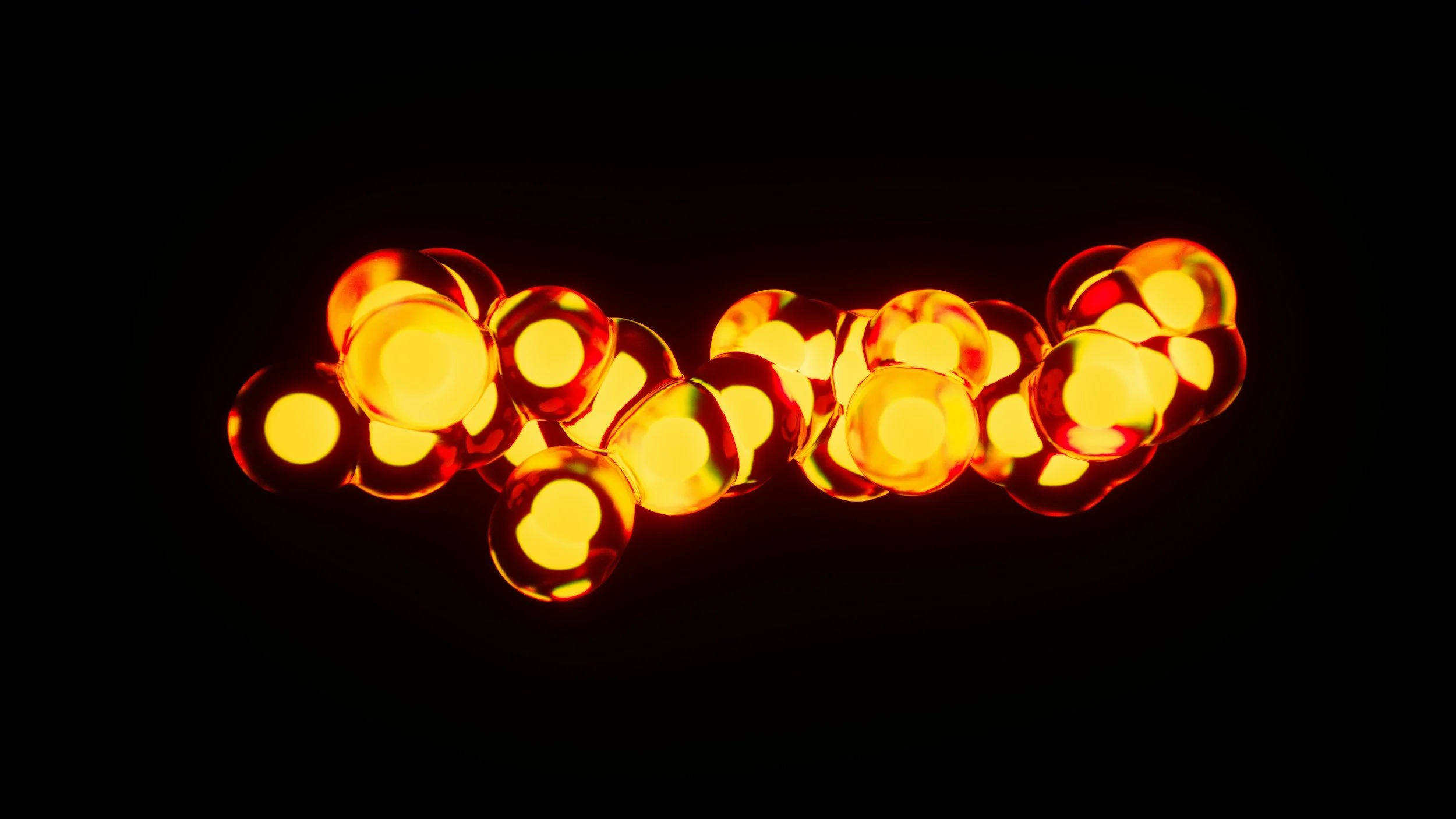 A close-up of glowing, orange and red glass spheres resembling beads, illuminated against a black background.
