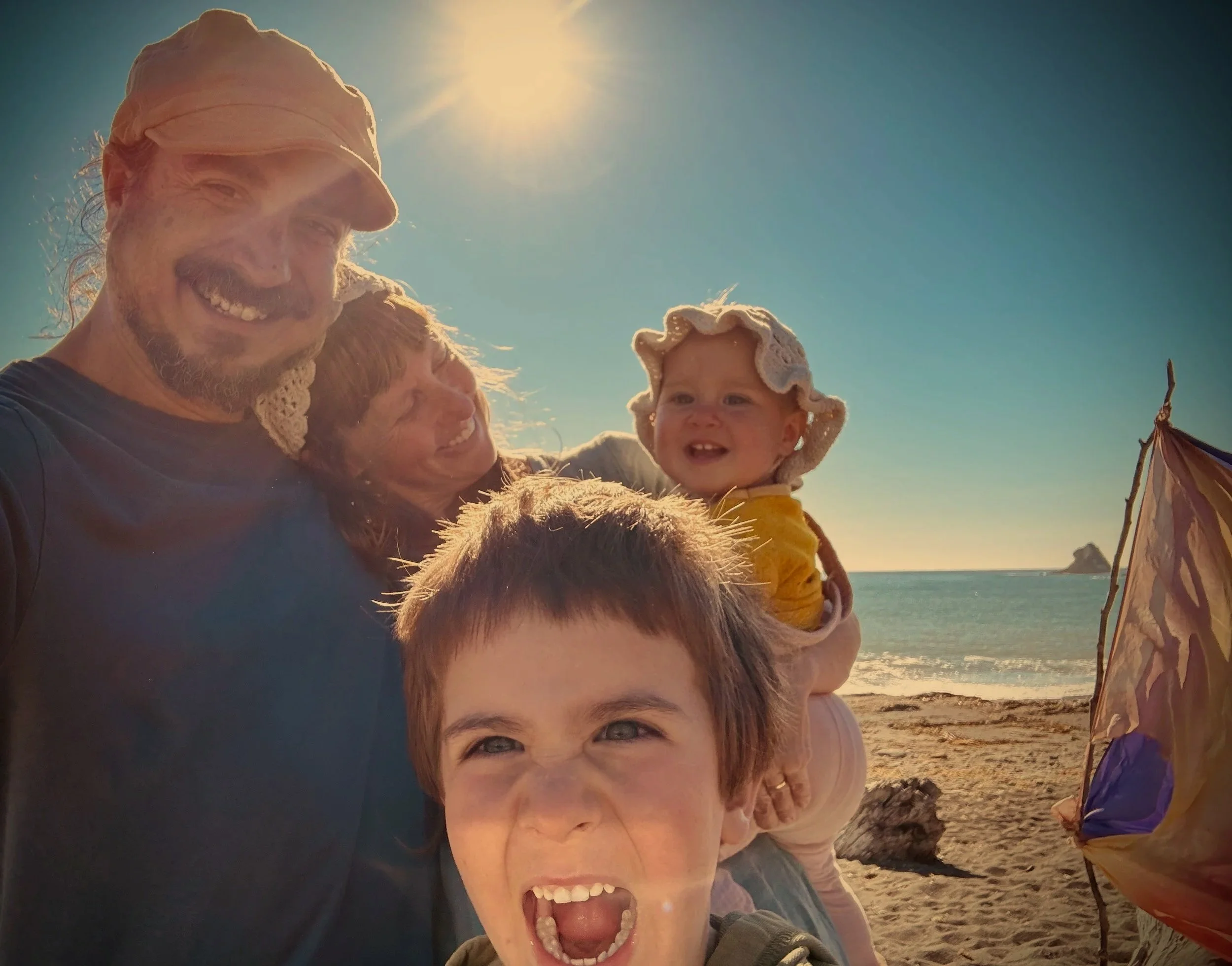 A family of four at the beach enjoying a sunny day, with a kite on the sand.