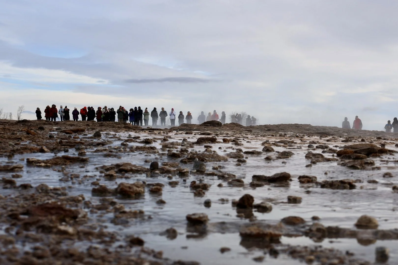A group of people standing on a rocky landscape with mist in the background and cloudy sky overhead.