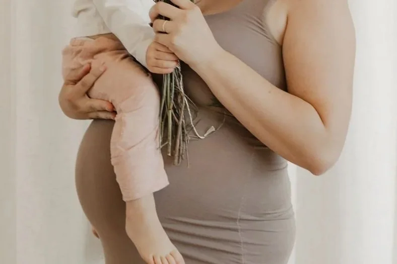 Woman holding a child, showing her pregnant belly.