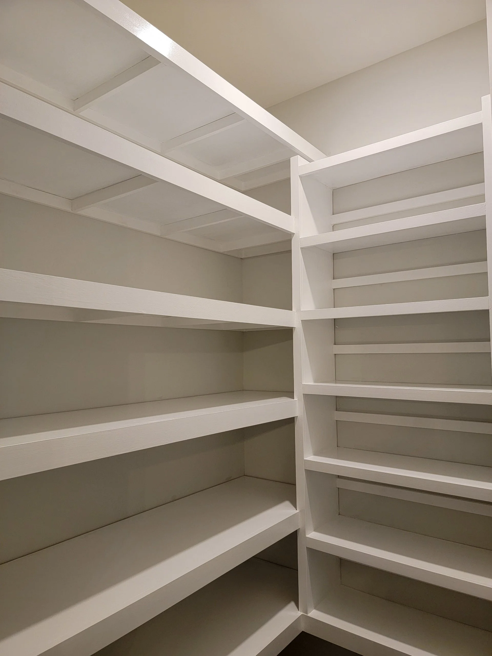 Empty white walk-in pantry with multiple shelves on both sides.
