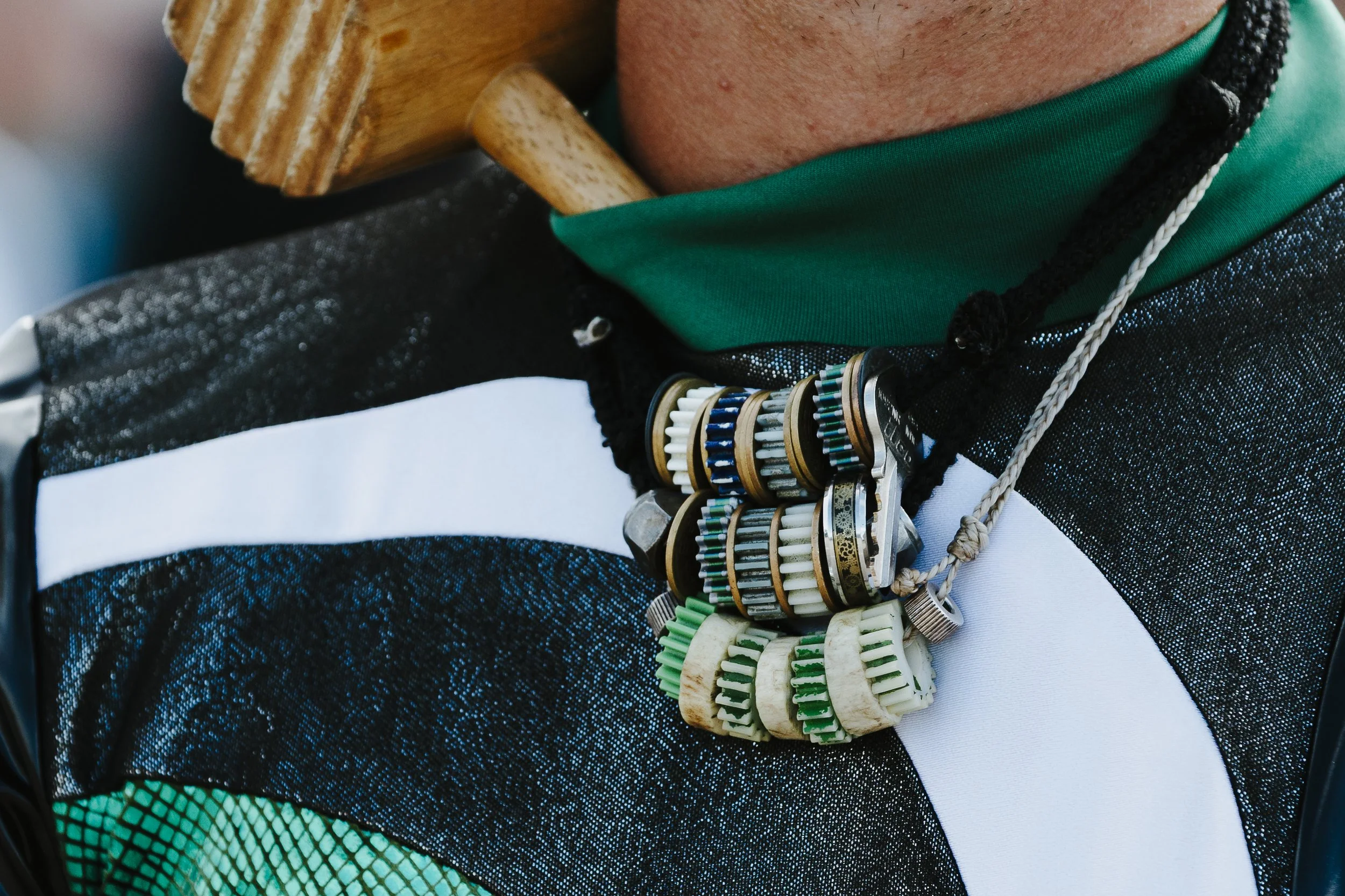 Close-up of a person wearing a necklace made of ammunition cartridges and a wooden object resting on their shoulder.