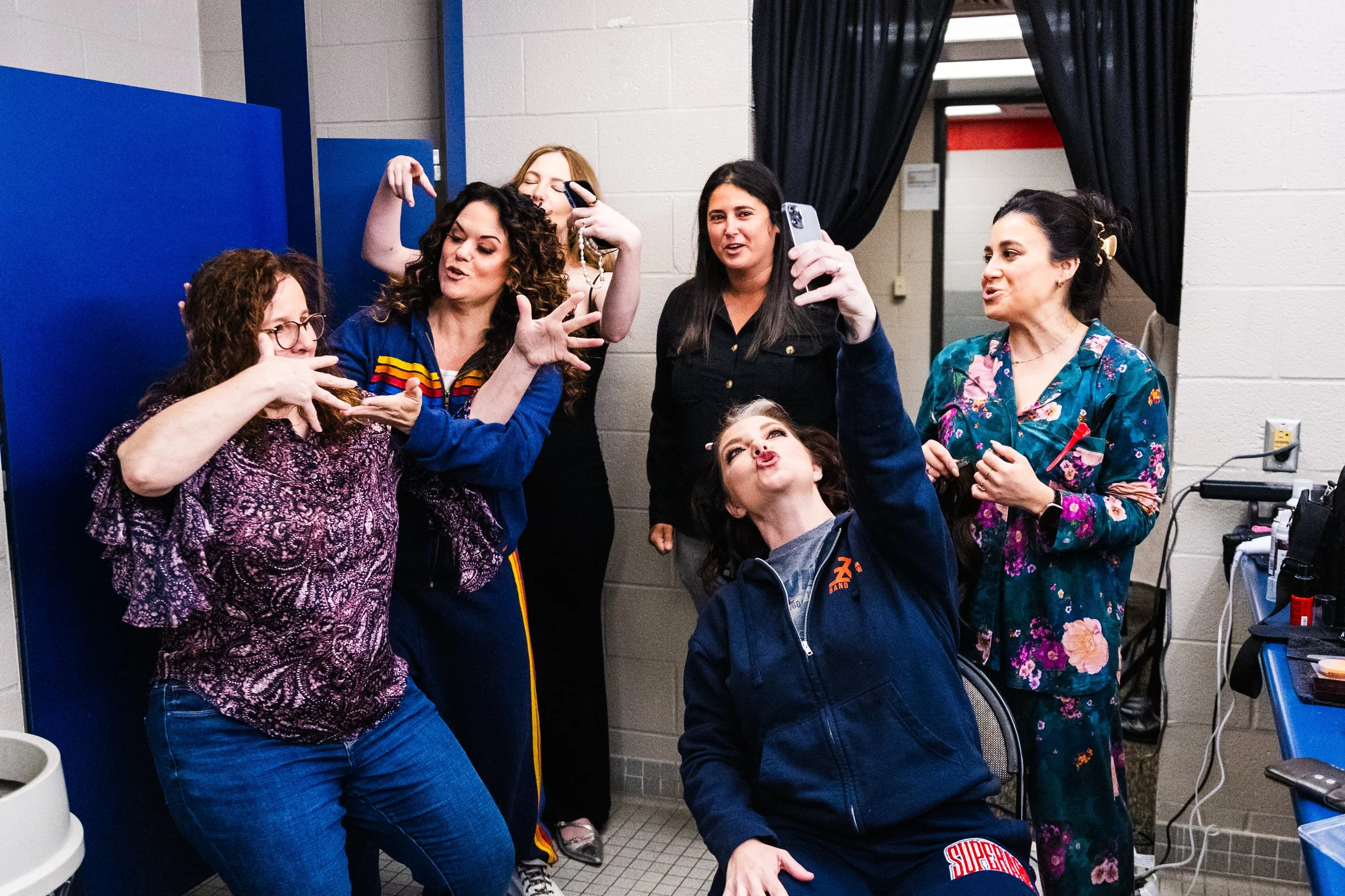 Ashley McBryde with a group of women in colorful clothing taking selfies and posing for photos together in a room with a brick wall and blue partitions.