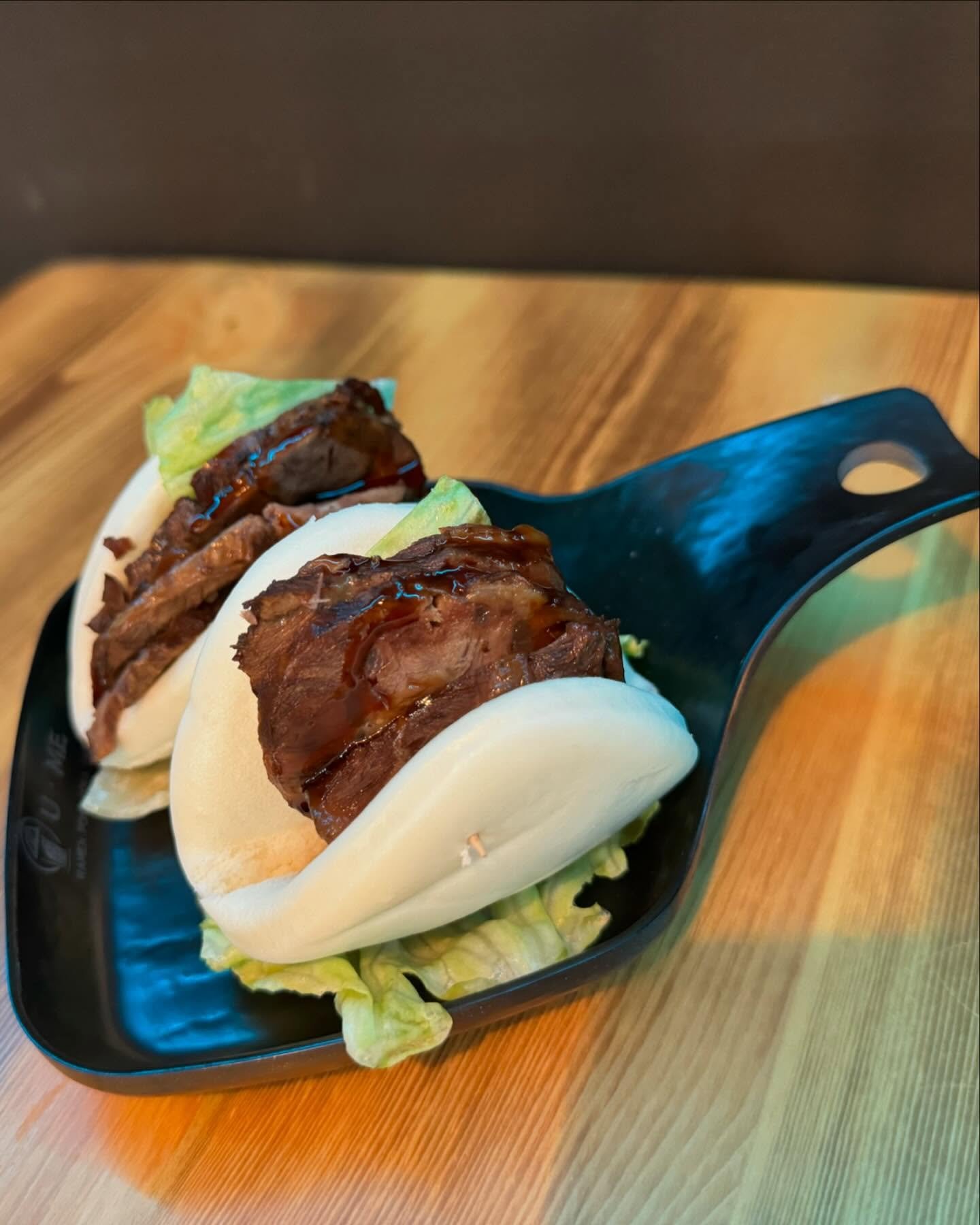 Two bao buns with beef, lettuce, and sauce on a black plate.