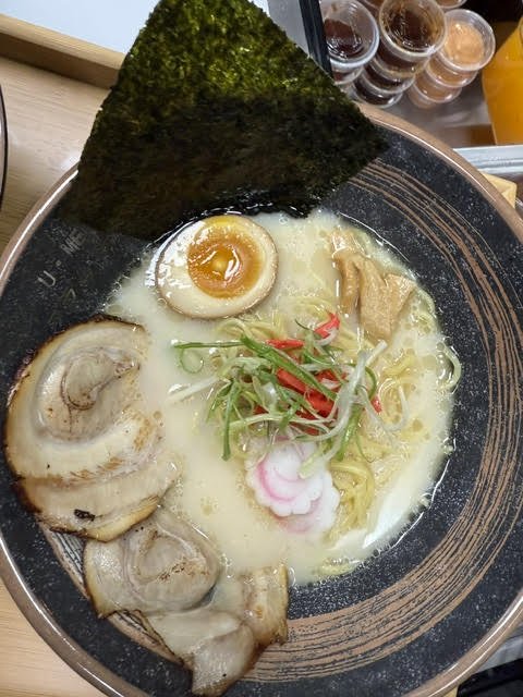 Bowl of ramen with broth, sliced pork, half a boiled egg, narutomaki, seaweed, and scallions.