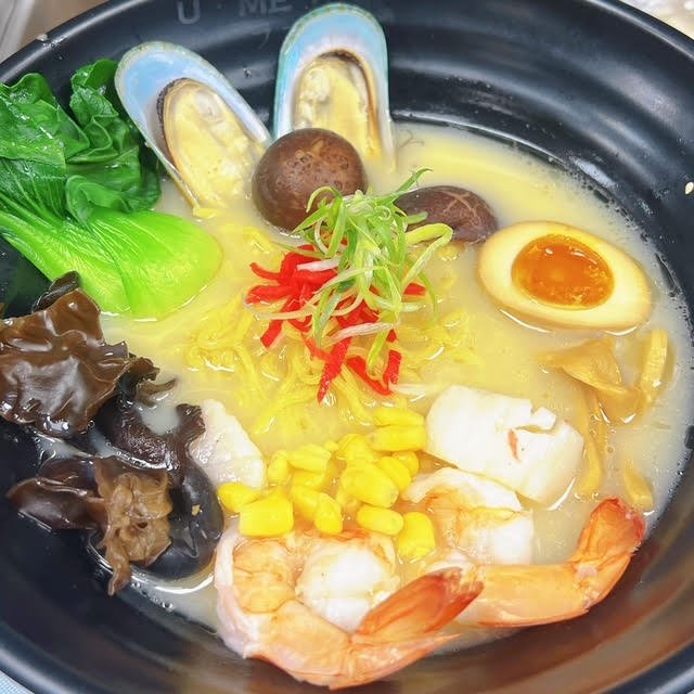 Seafood ramen with shrimp, mussels, corn, bok choy, shiitake mushrooms, wood ear fungus, half-boiled egg, and green onions in a creamy broth.