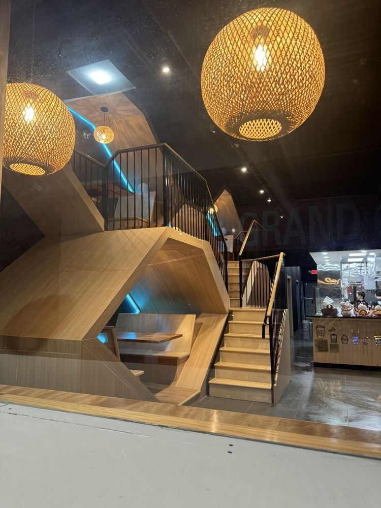 Modern indoor cafe with wooden seating, staircase, and woven light fixtures.