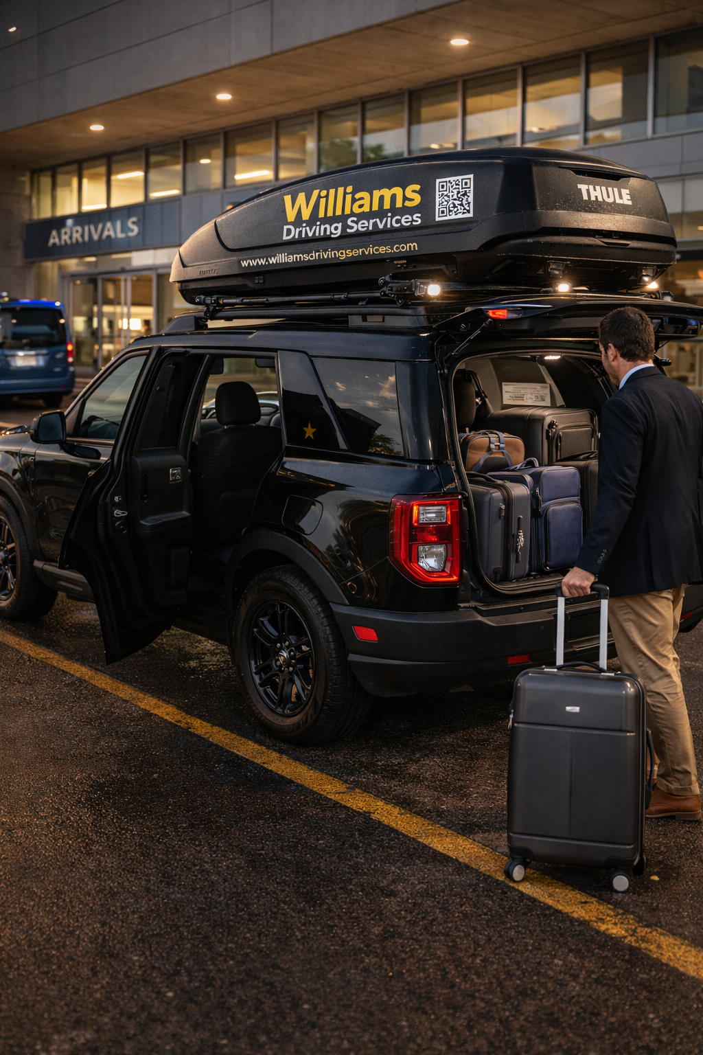 Man with brown hair in a suit loading suitcases into the trunk of a black SUV at an airport arrivals terminal during evening or early morning, with a rooftop cargo box labeled 'Williams Driving Services' and a sign reading 'ARRIVALS' in the background.