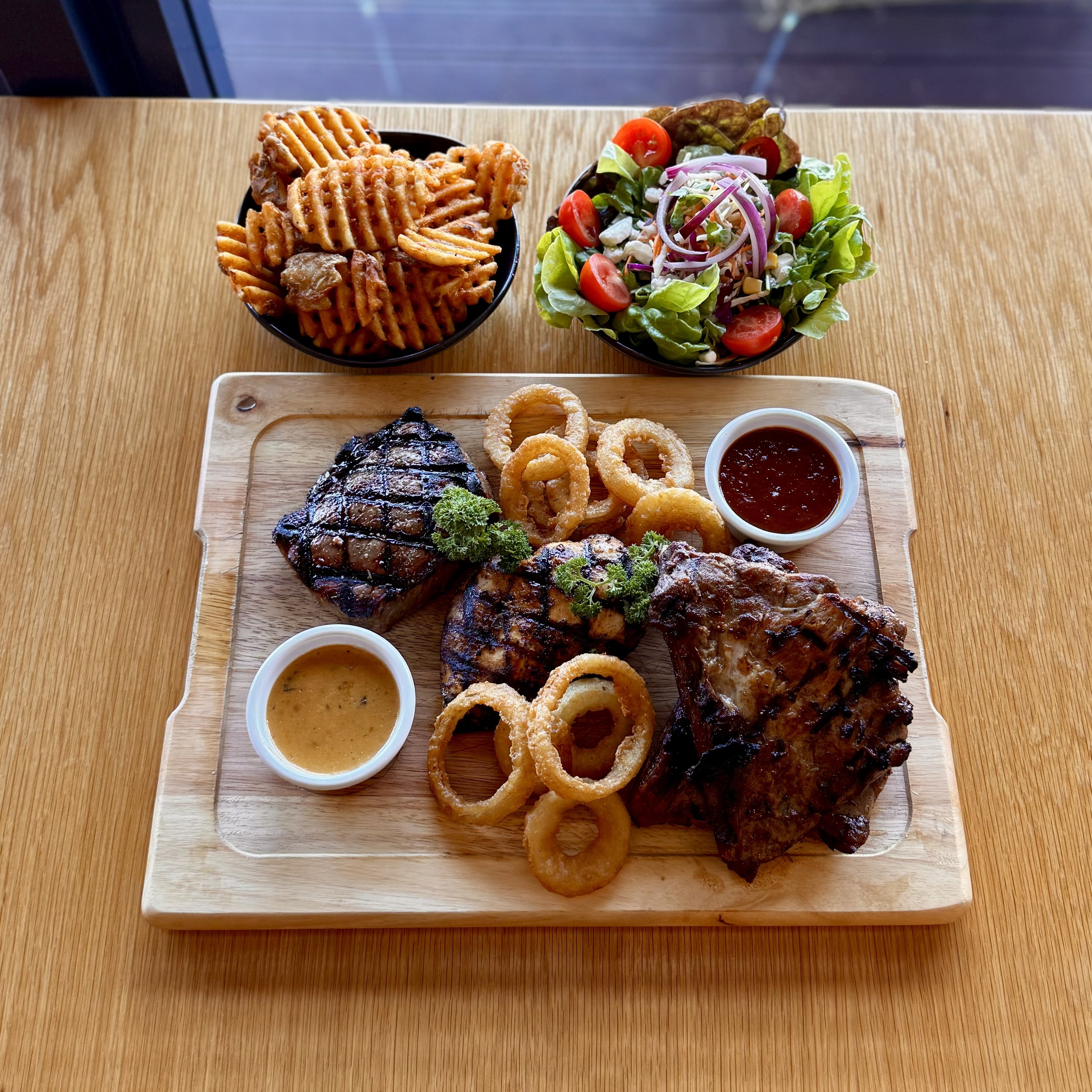 A close-up of a juicy grilled steak with grill marks being cooked on a barbecue grill with flames. The text overlay reads: 'IT'S BACK MEAL DEAL FOR 2. Not valid with any other offers or specials.'
