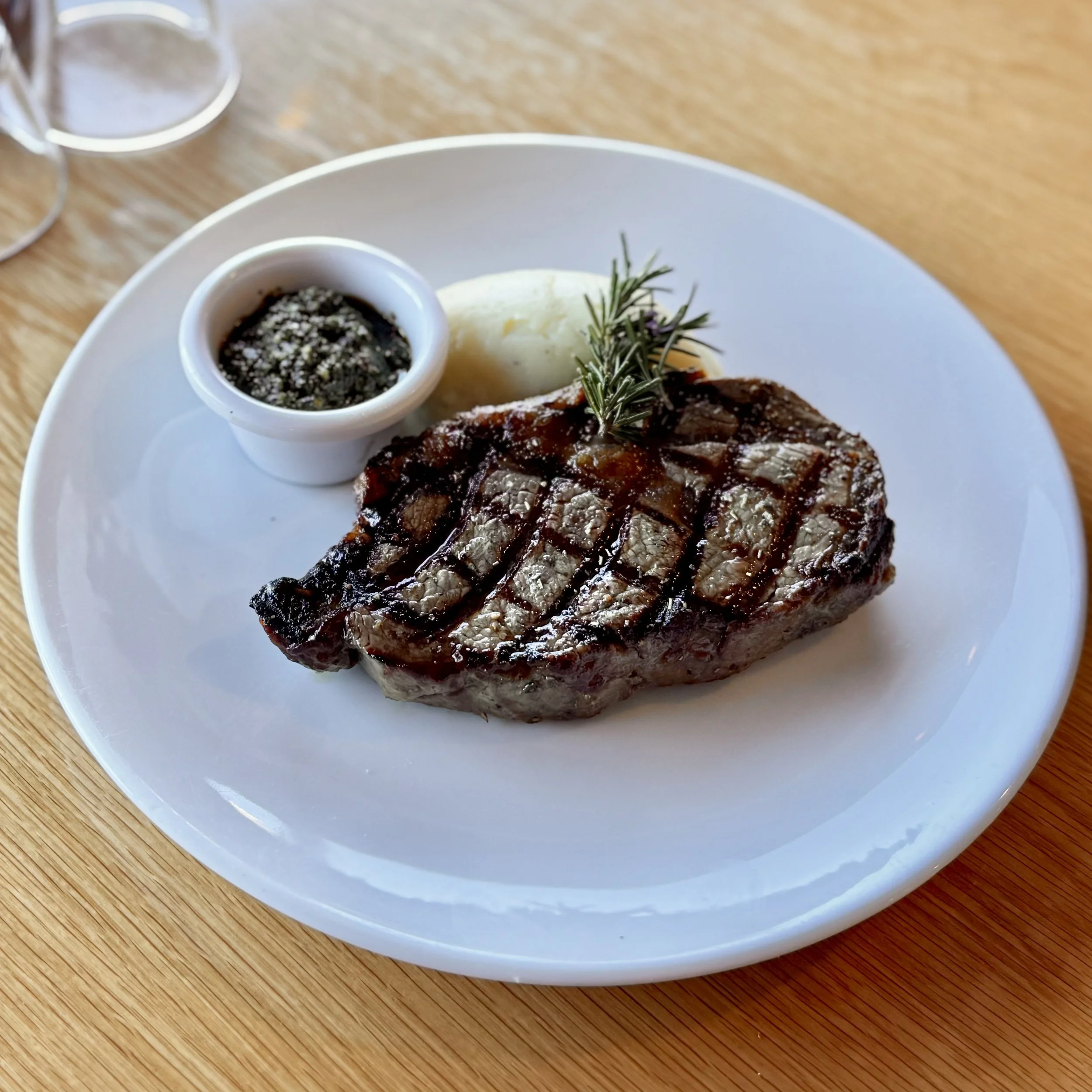  steak served with a side of mashed potatoes and a small dish of herb sauce.ce, served over mashed potatoes with a sprig of rosemary and green garnish.