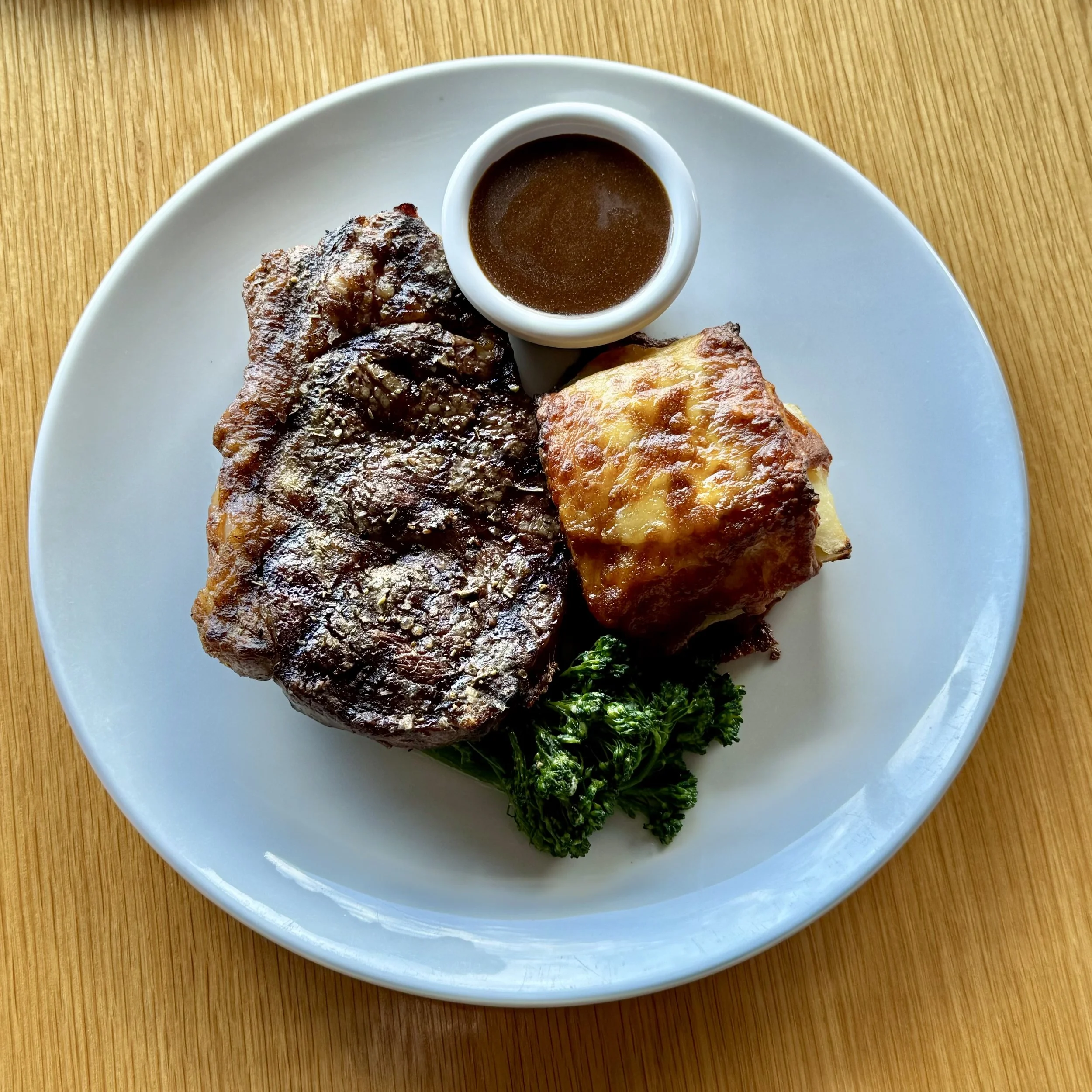 steak served with a side of mashed potatoes and a small dish of herb sauce.ce, served over mashed potatoes with a sprig of rosemary and green garnish.