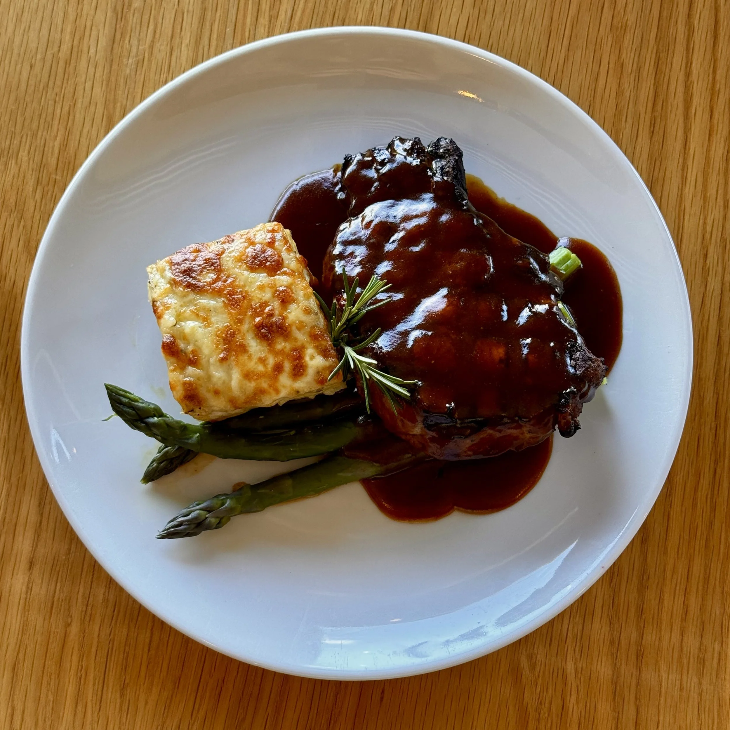 A plate of grilled steak topped with a dark sauce, served over mashed potatoes with a sprig of rosemary and green garnish.
