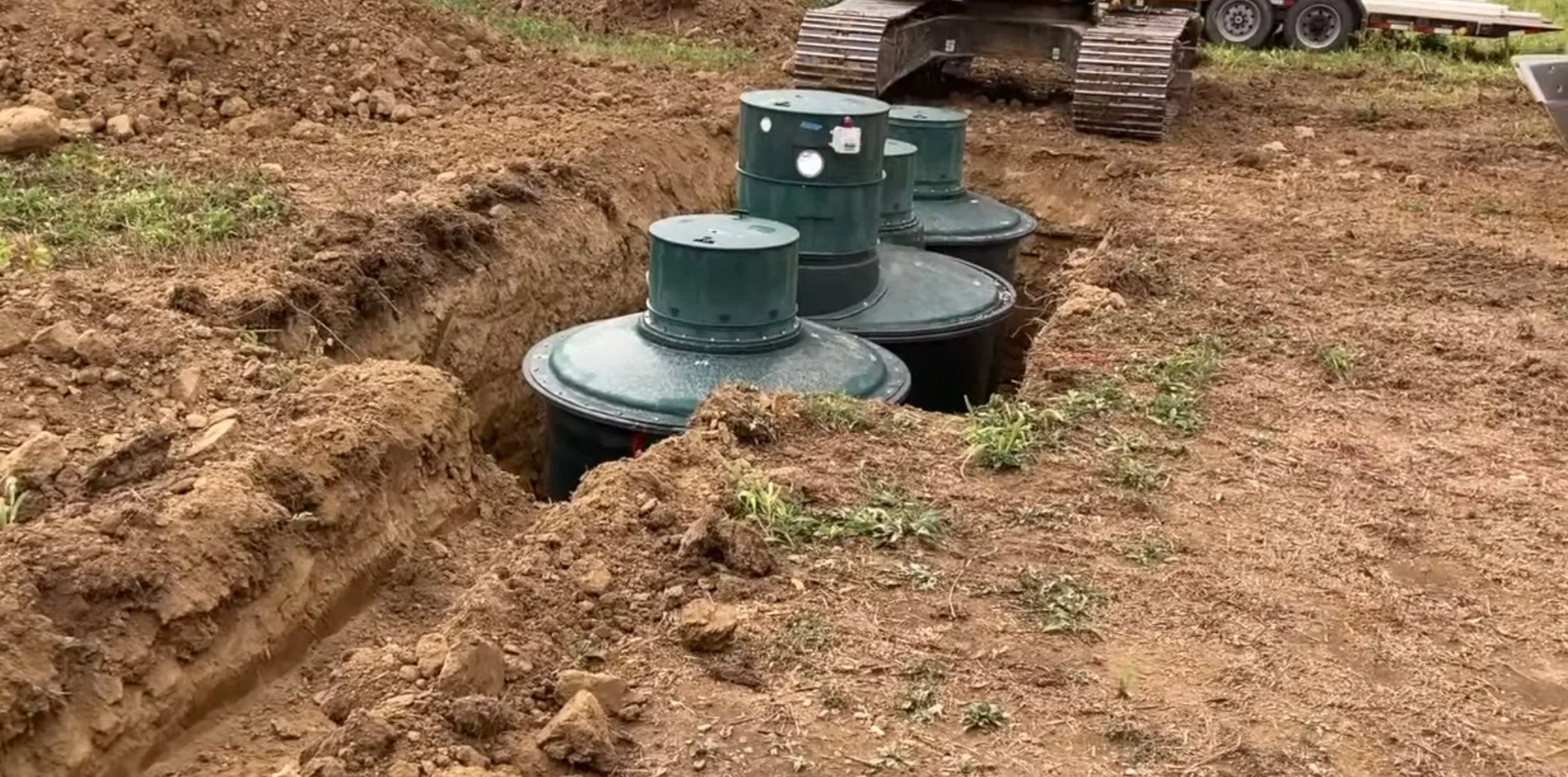 Hydro-action underground septic tanks being installed in a dug trench in a rural area.