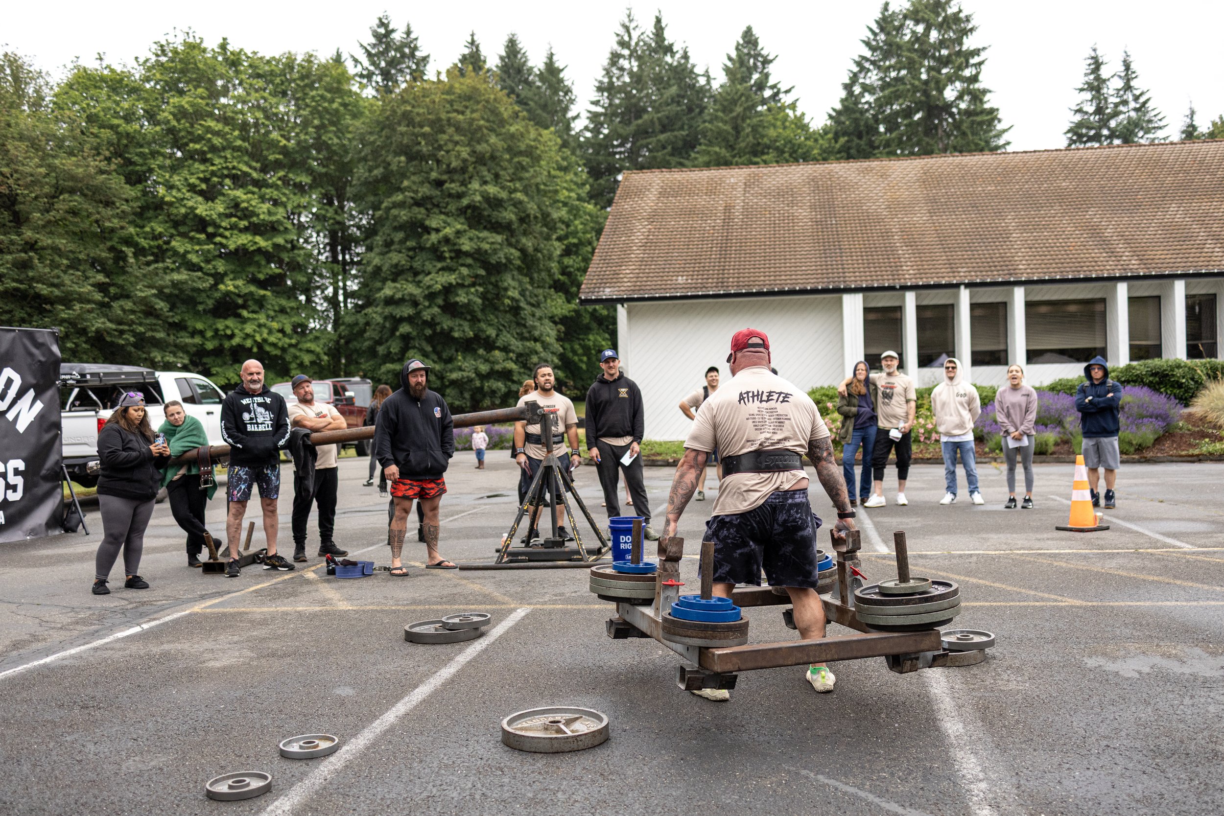 A strongman competition outdoors where a man with tattoos is lifting weights on a frame while an audience watches.