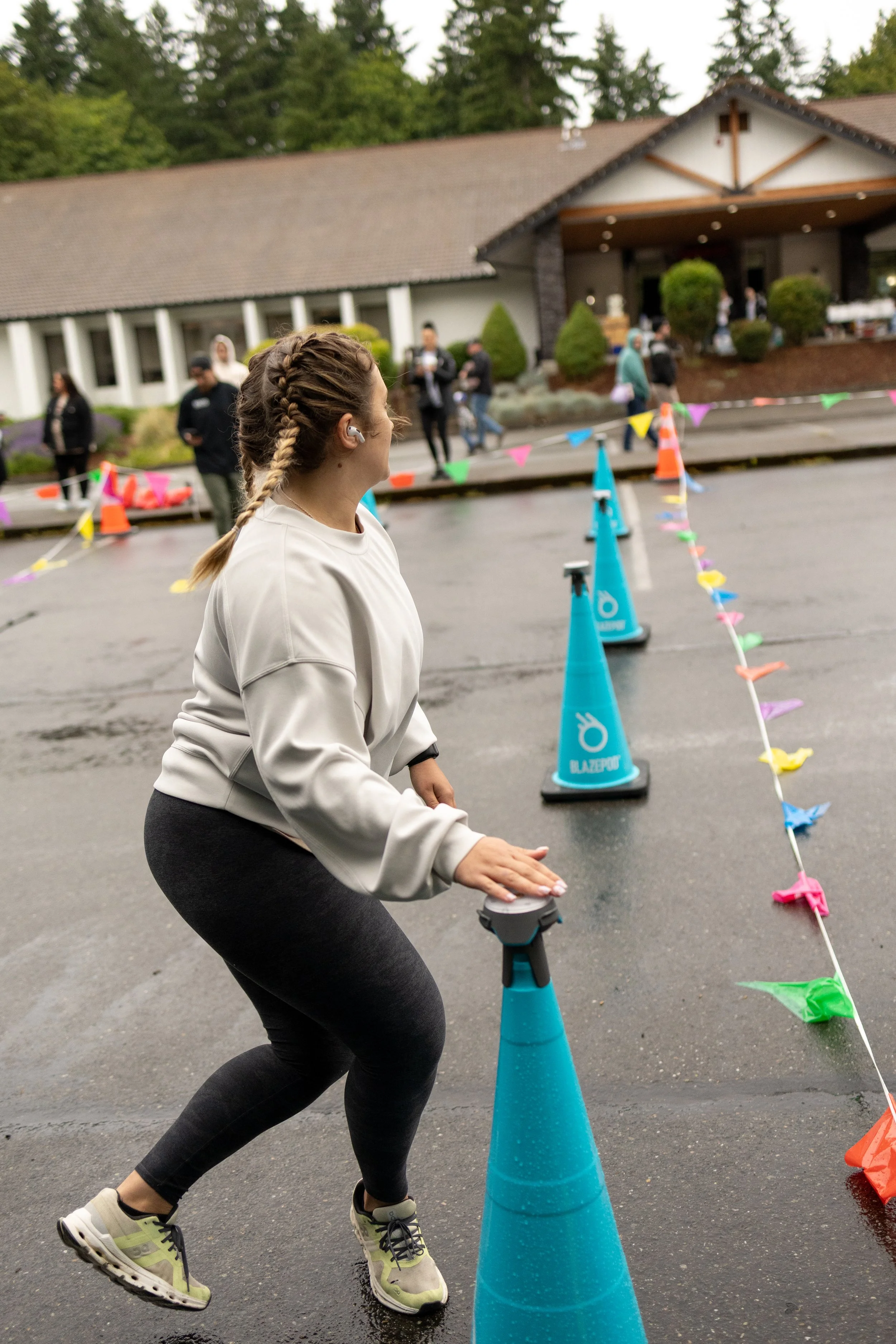 A woman with braided hair and gray sweatshirt participating in the outdoor Samson Fest event, pushing a cone along a line marked with colorful flags.