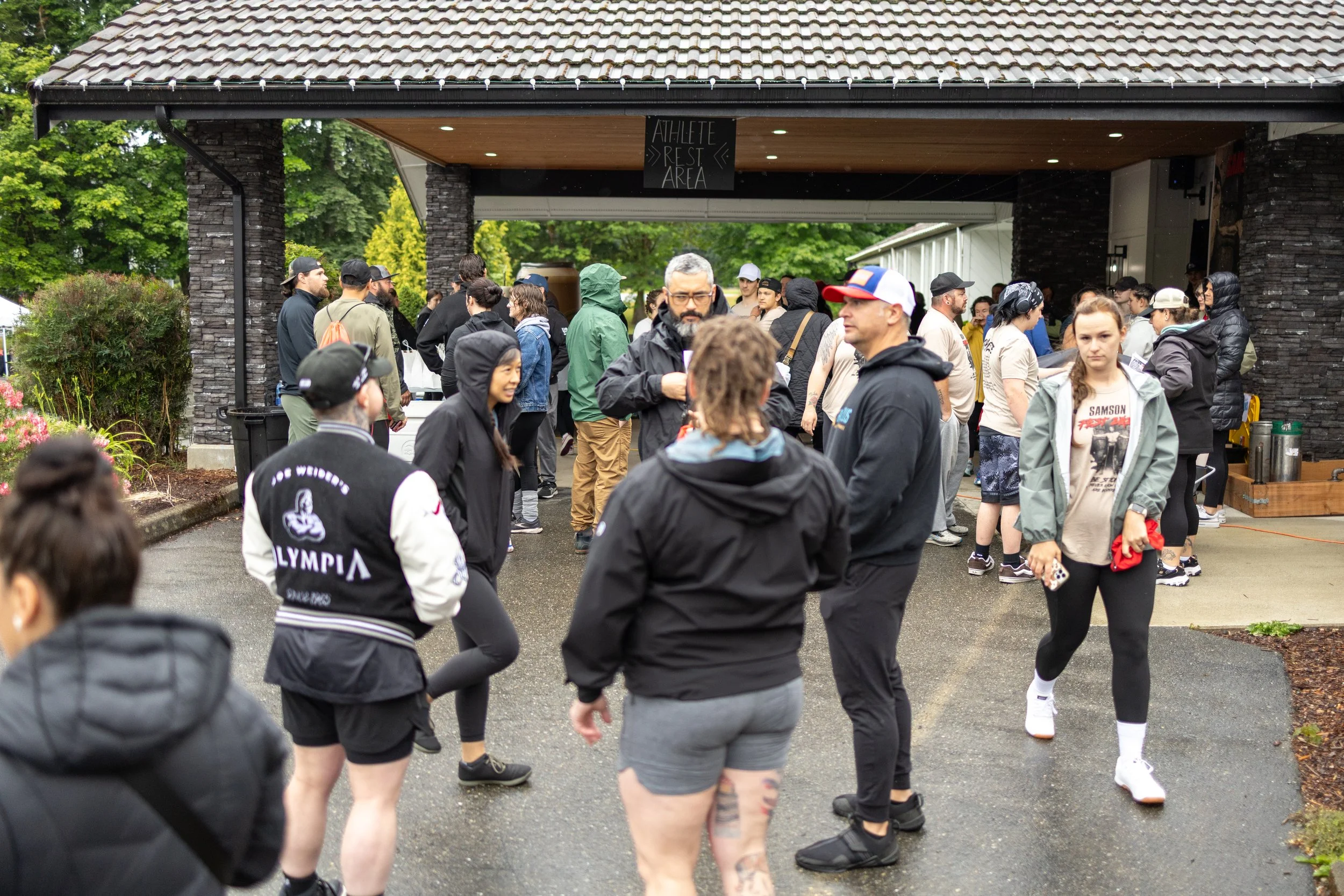 Group of people gathered outdoors near the 'Athlete Rest Area', some wearing athletic clothing, as they socialize and wait for Samson Fest to begin