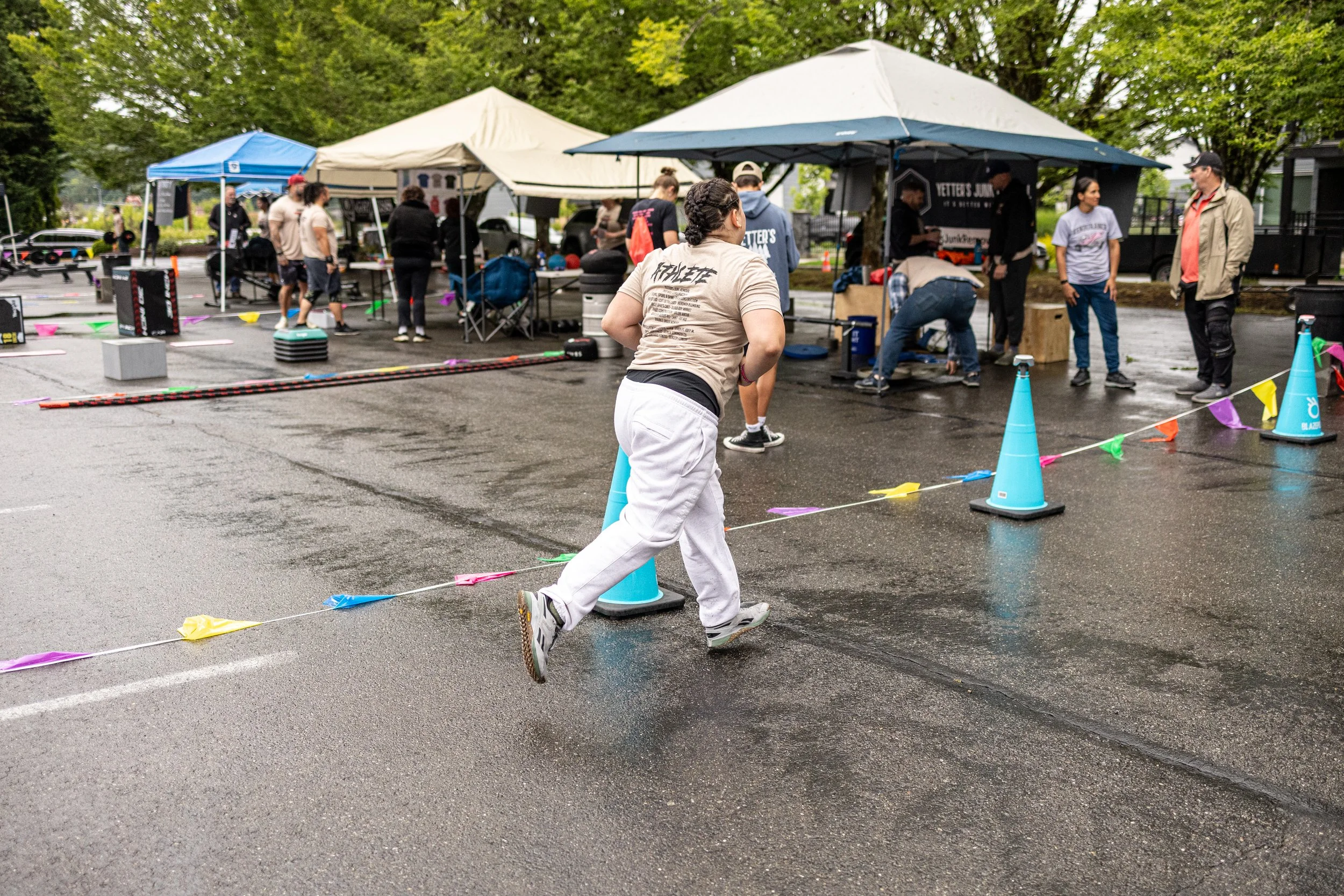 A woman running in a parking lot during an outdoor event on a rainy day, with tents and people in the background.
