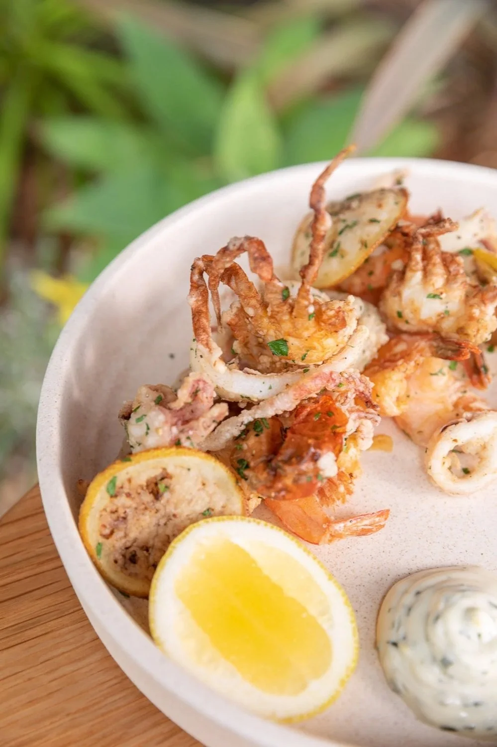 Fried calamari with lemon wedges and dipping sauce served on a white plate.