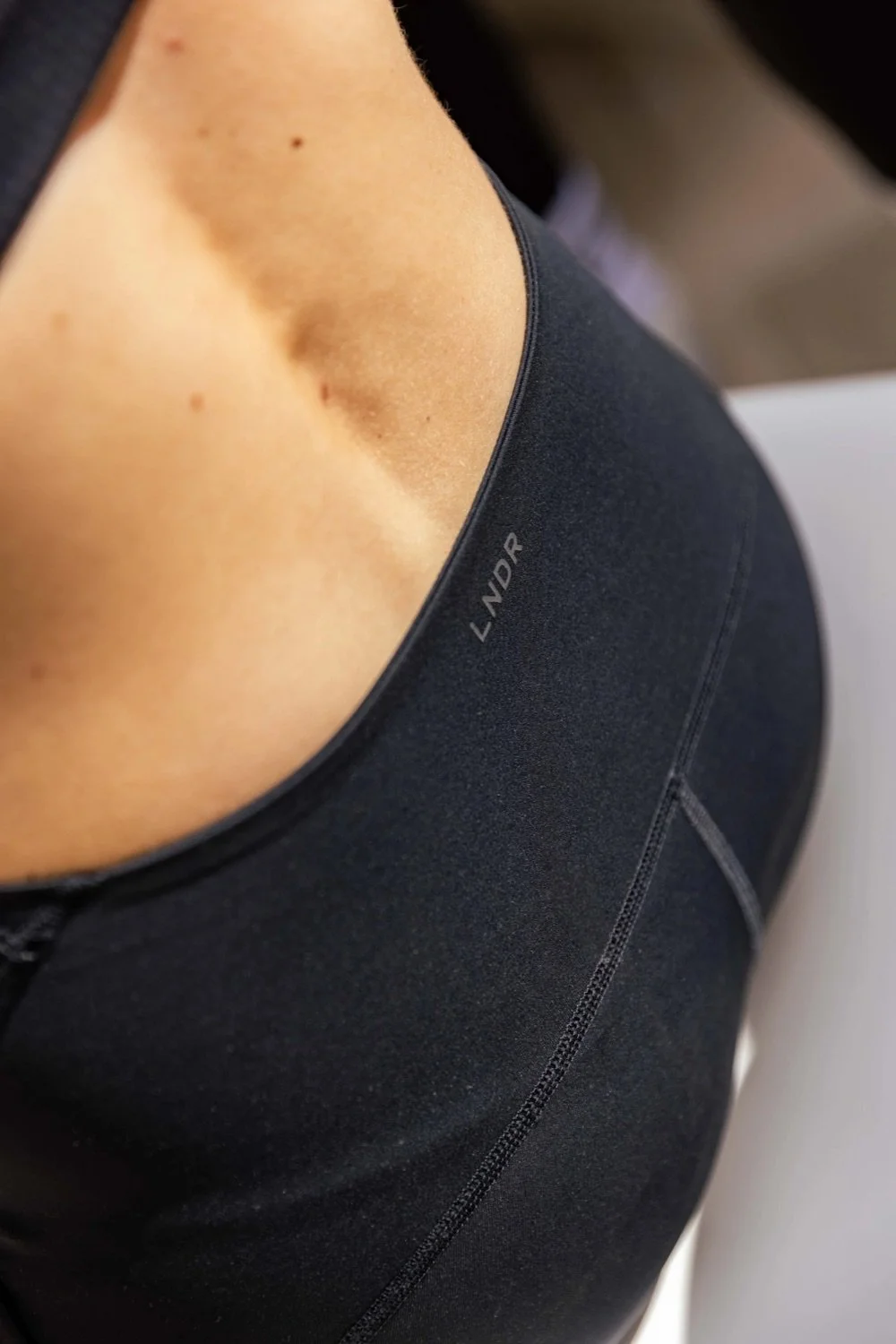 Close-up of a person wearing a black Lululemon sports bra and black athletic leggings, showing a portion of their upper back and shoulder.