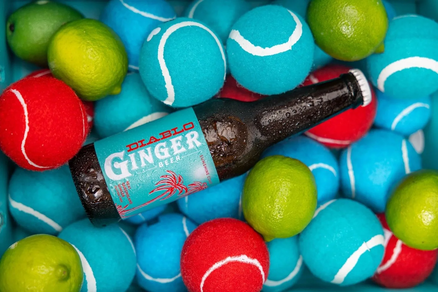 A bottle of Diablo Ginger Beer surrounded by colorful tennis balls and limes.