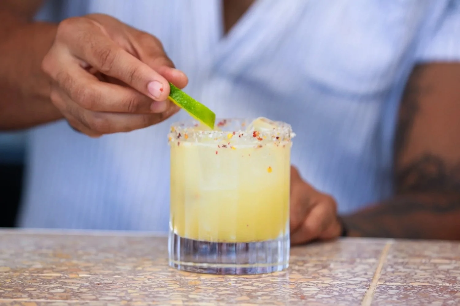 Person adding a lime wedge to a salted rim margarita in a short glass.