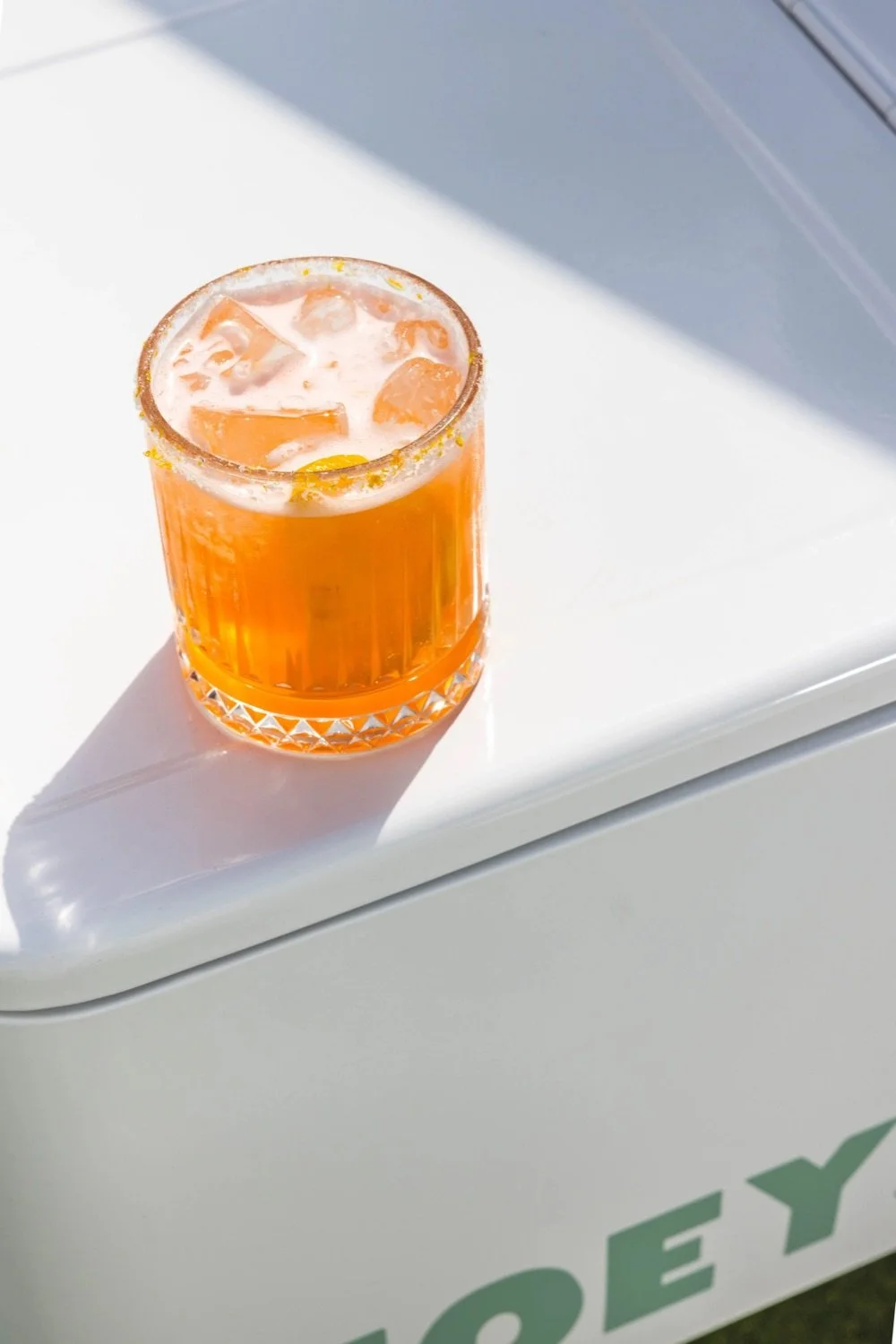 A glass of orange-colored drink with ice cubes on a white surface.