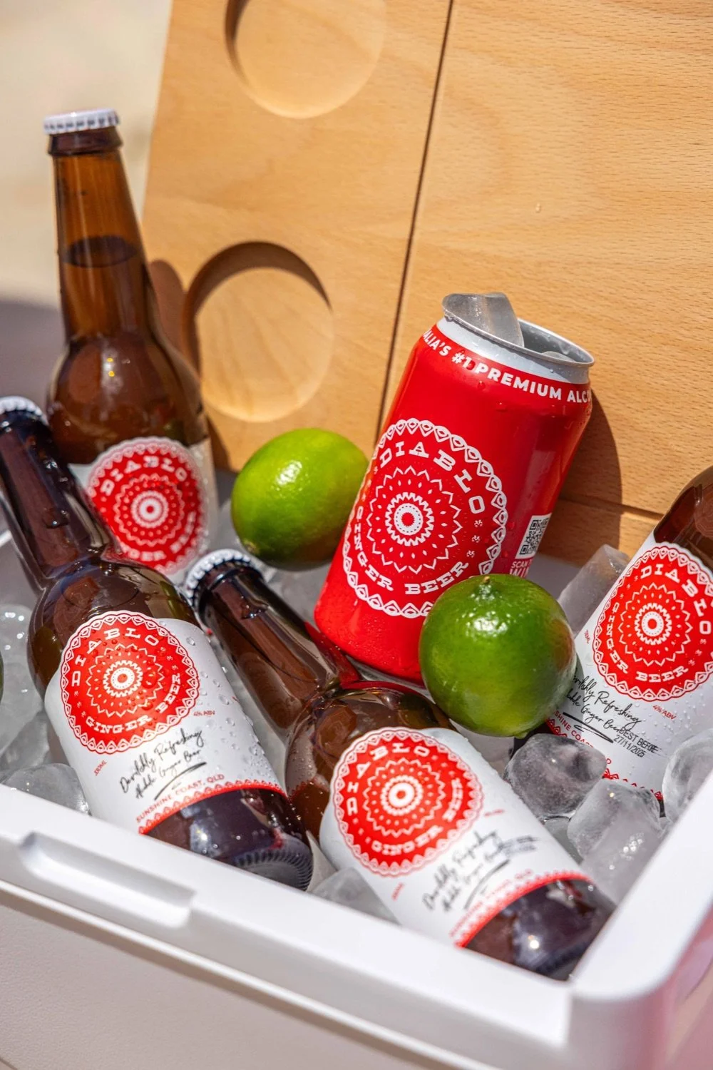 Cooler contains several bottles of ginger beer, two limes, and ice.
