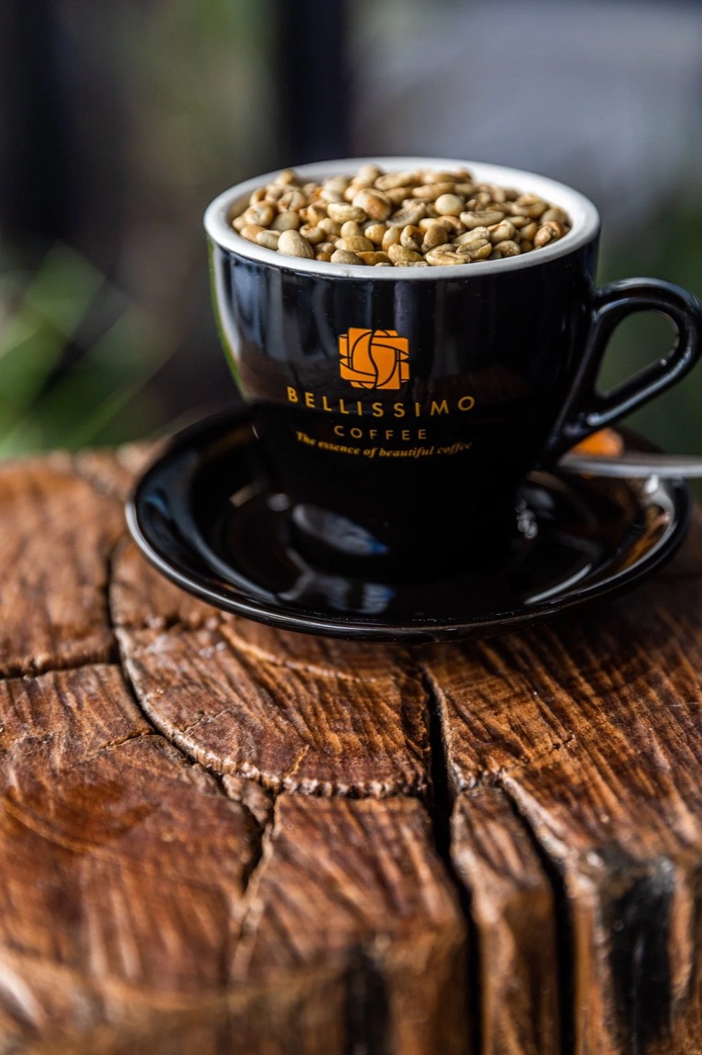 Black coffee cup filled with coffee beans, placed on a matching saucer on a wooden surface.