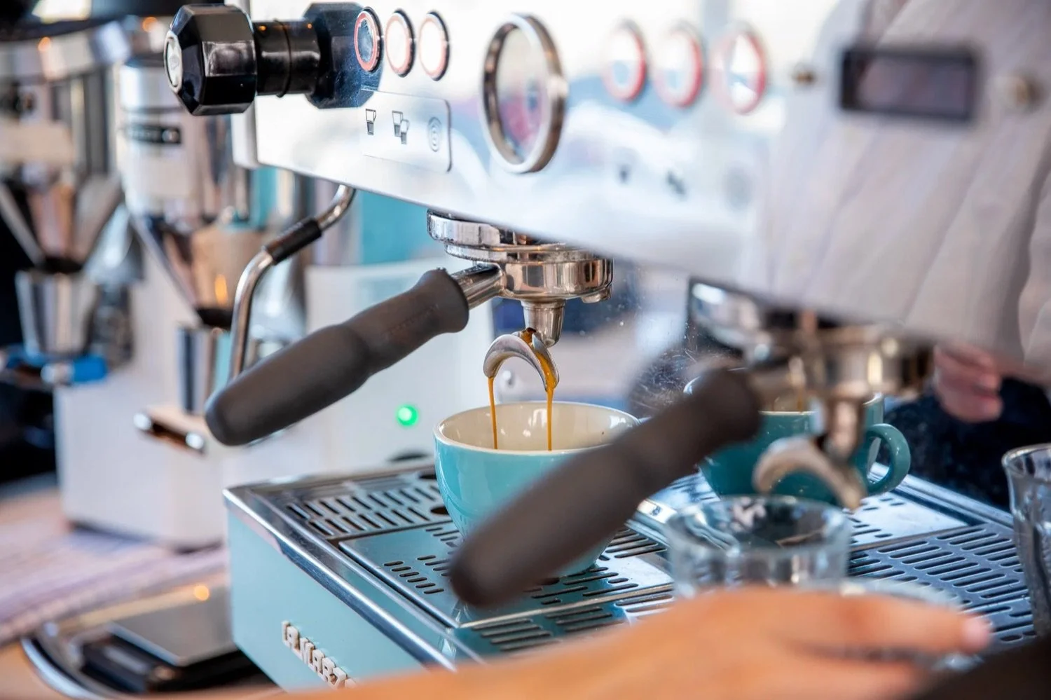 Close-up of an espresso machine pouring coffee into a light blue mug with a second mug nearby.