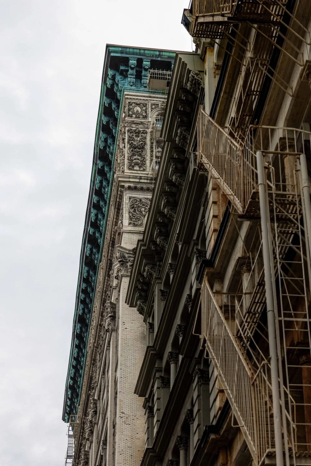 Close-up view of the side of a historic multi-story building with ornate architectural details and fire escape stairs, viewed from below.